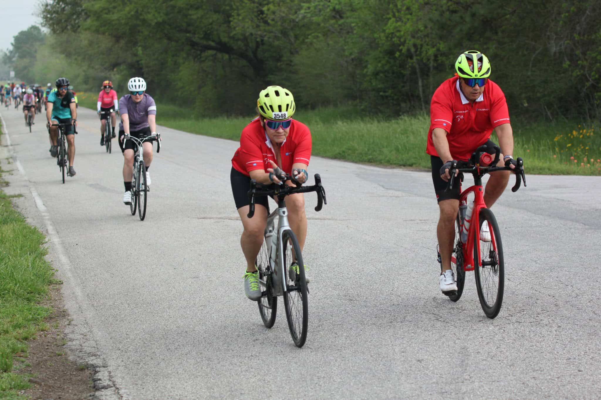 Scenic bike ride with cyclists on a rural road during daytime, part of Bluebonnet Express cycling event.
