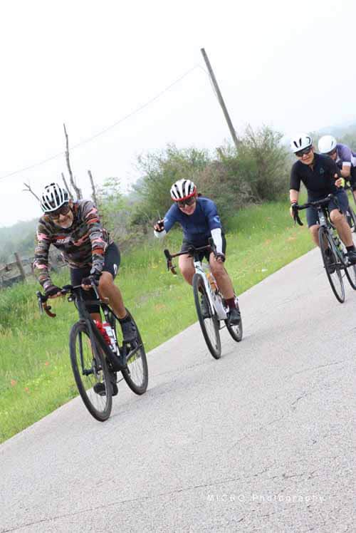 Velo cyclists group riding on scenic rural road during daytime.