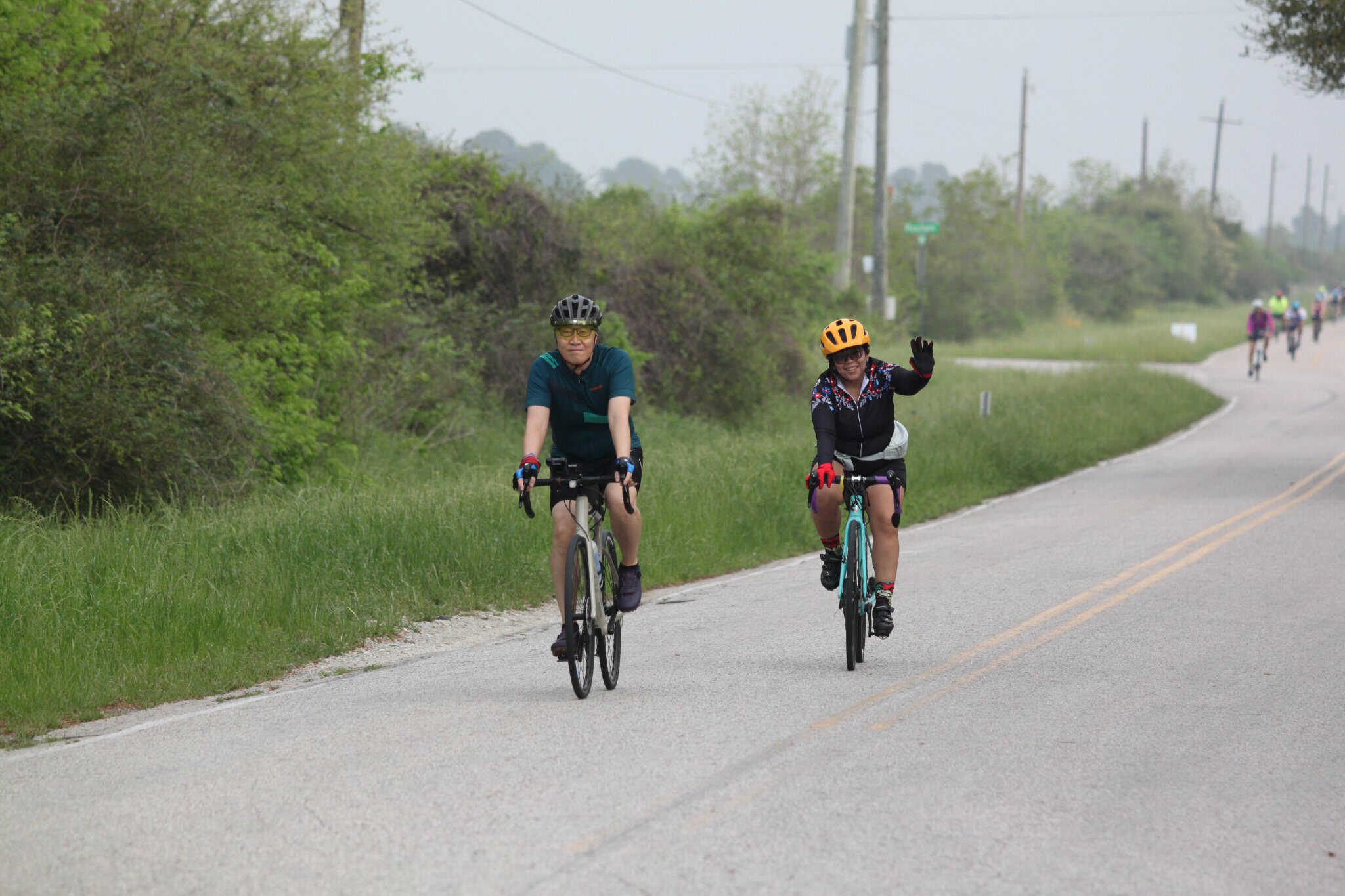 Scenic bike ride along rural road with two cyclists waving, part of Bluebonnet Express event.