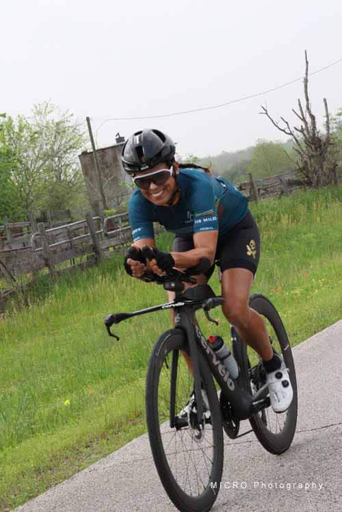 Bright female cyclist smiling while riding a black road bike outdoors during daytime.