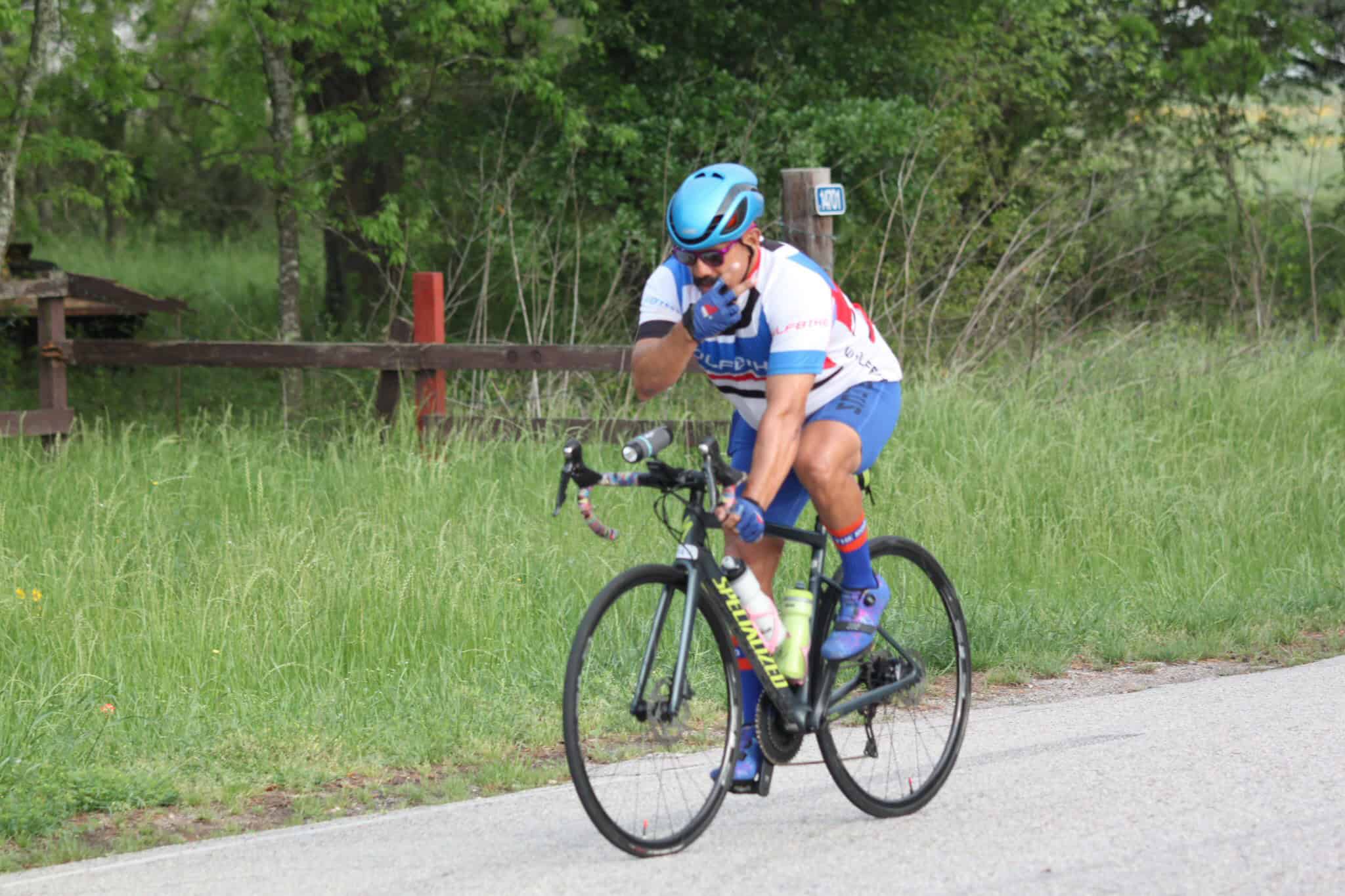 Vibrant cyclist wearing Bluebonnet Express jersey riding a road bike on scenic countryside trail.