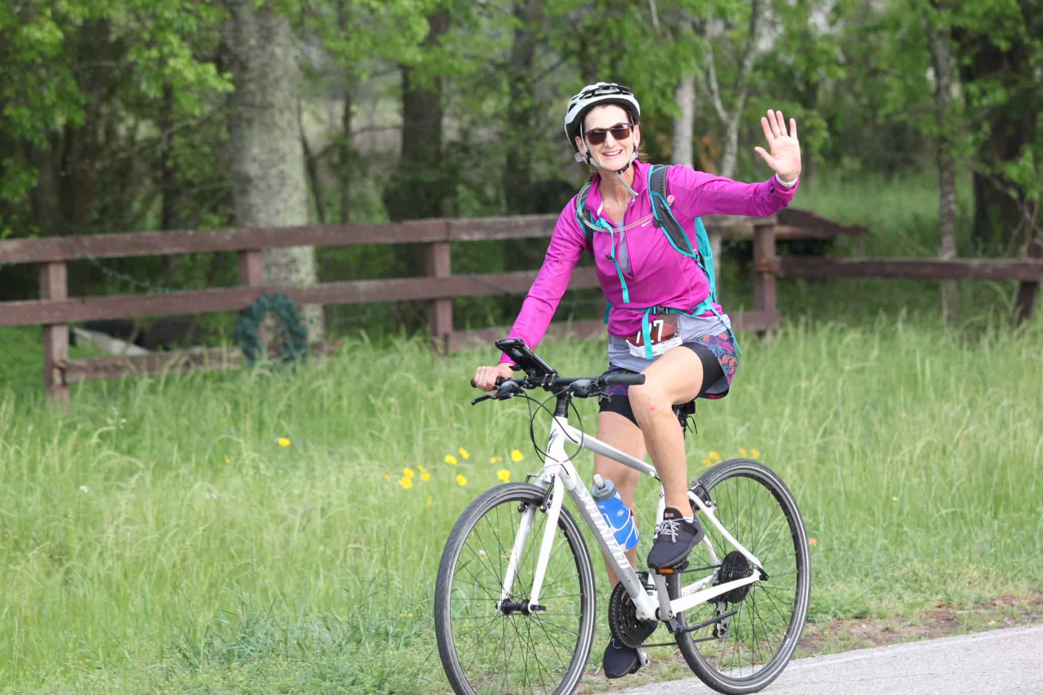 Vibrant woman riding a bicycle on a scenic trail with lush greenery and trees.