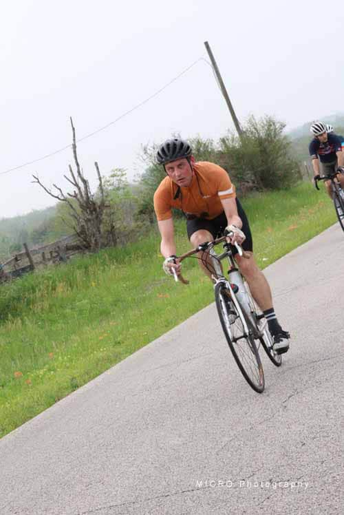 High-performance cyclist riding on scenic countryside road with lush greenery and overcast sky.