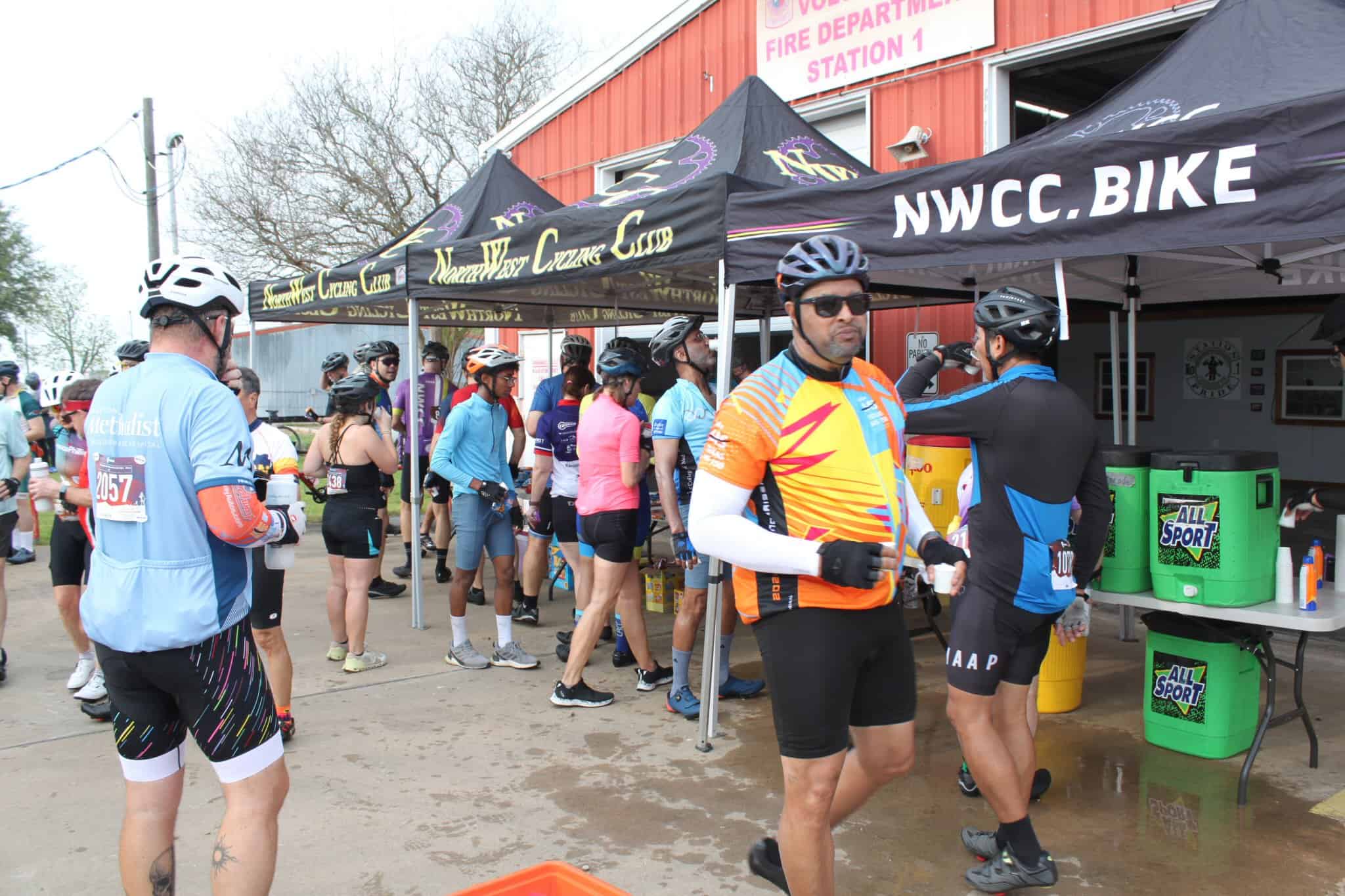 Cyclists gathering at Bluebonnet Express race event under NWCC Bike tent with hydration stations.
