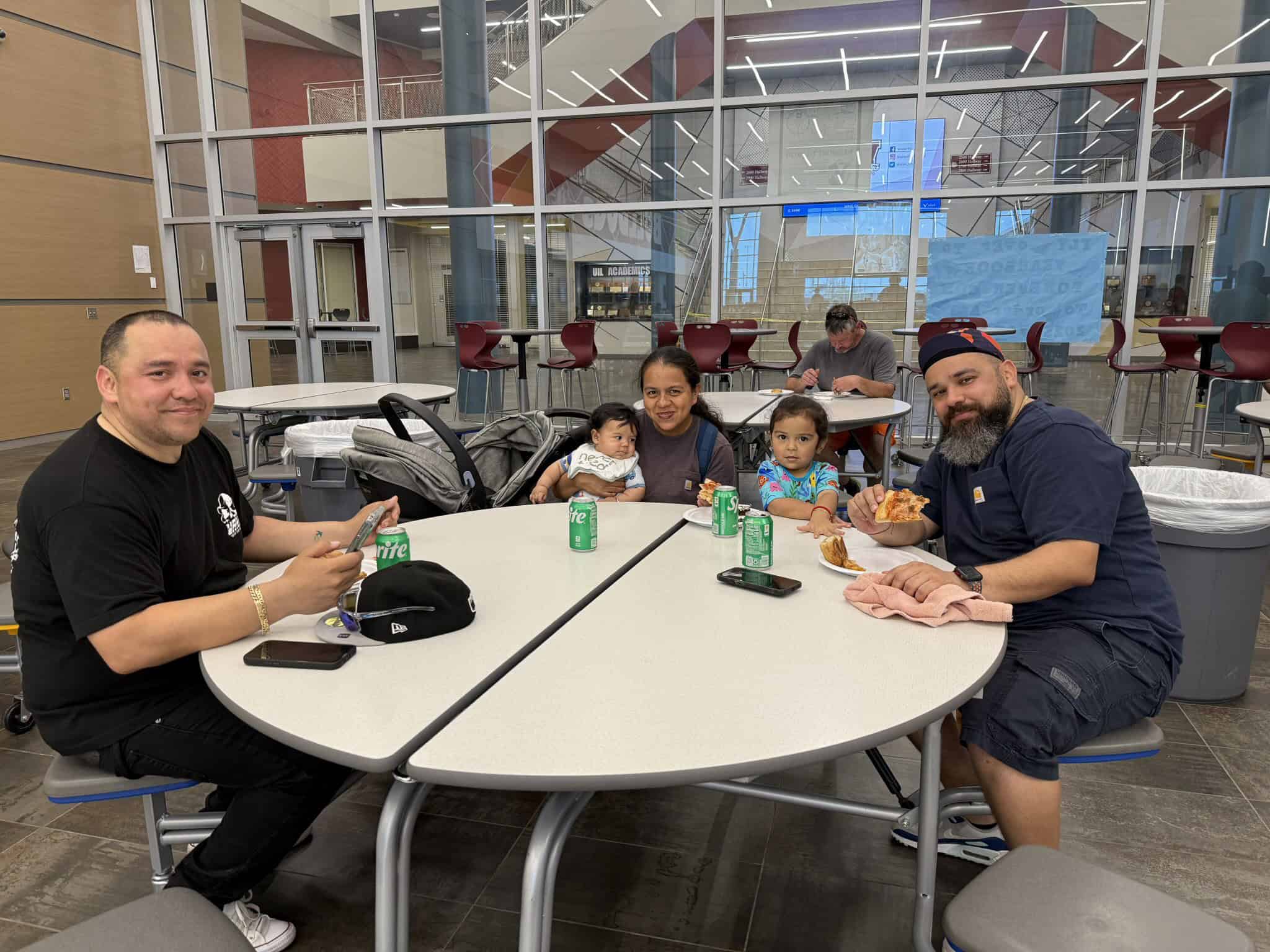 Bright airport interior with a group of smiling people enjoying pizza at a round table, showcasing travel and dining experience.