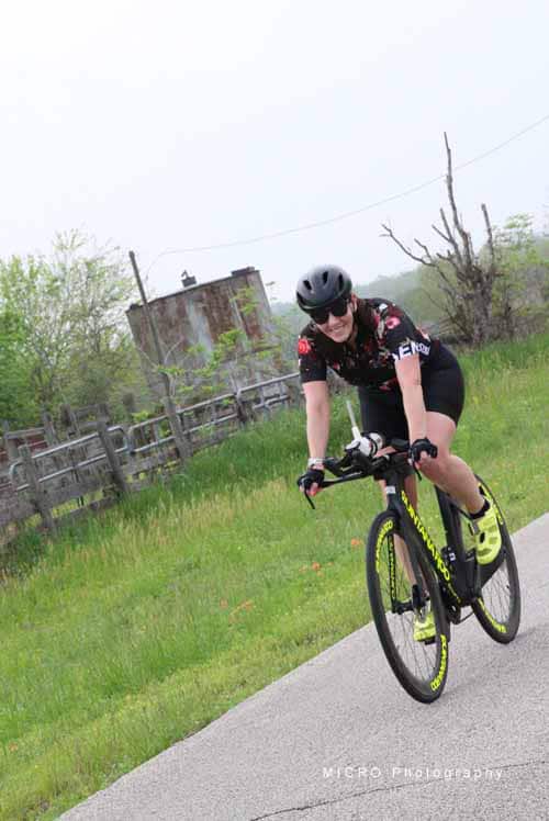 Bright female cyclist riding a black and yellow bike on a scenic country road, promoting Bluebonnet Express bike tours.
