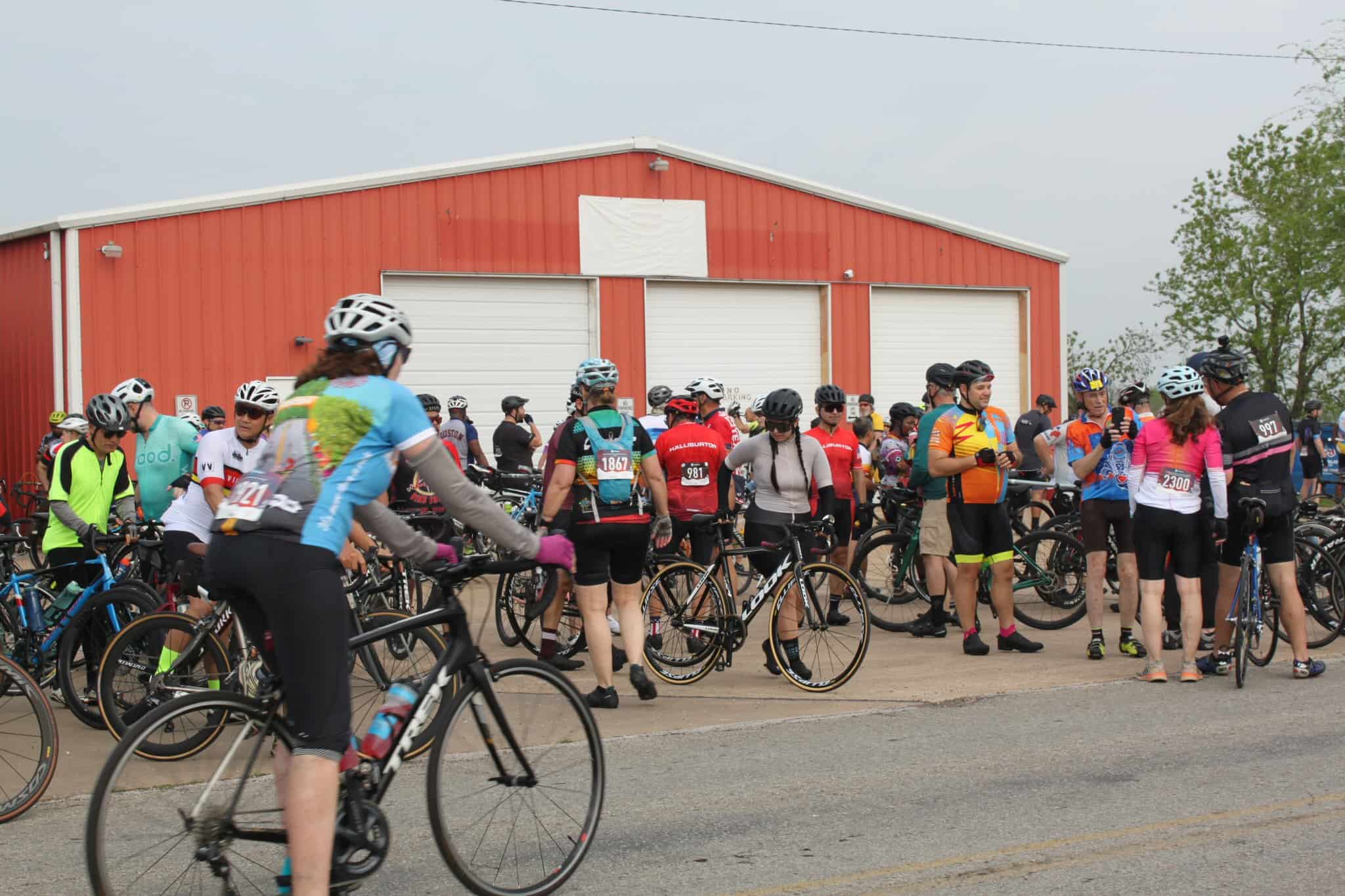 Cyclists gathering at the Bluebonnet Express bike race event outside a red barn.