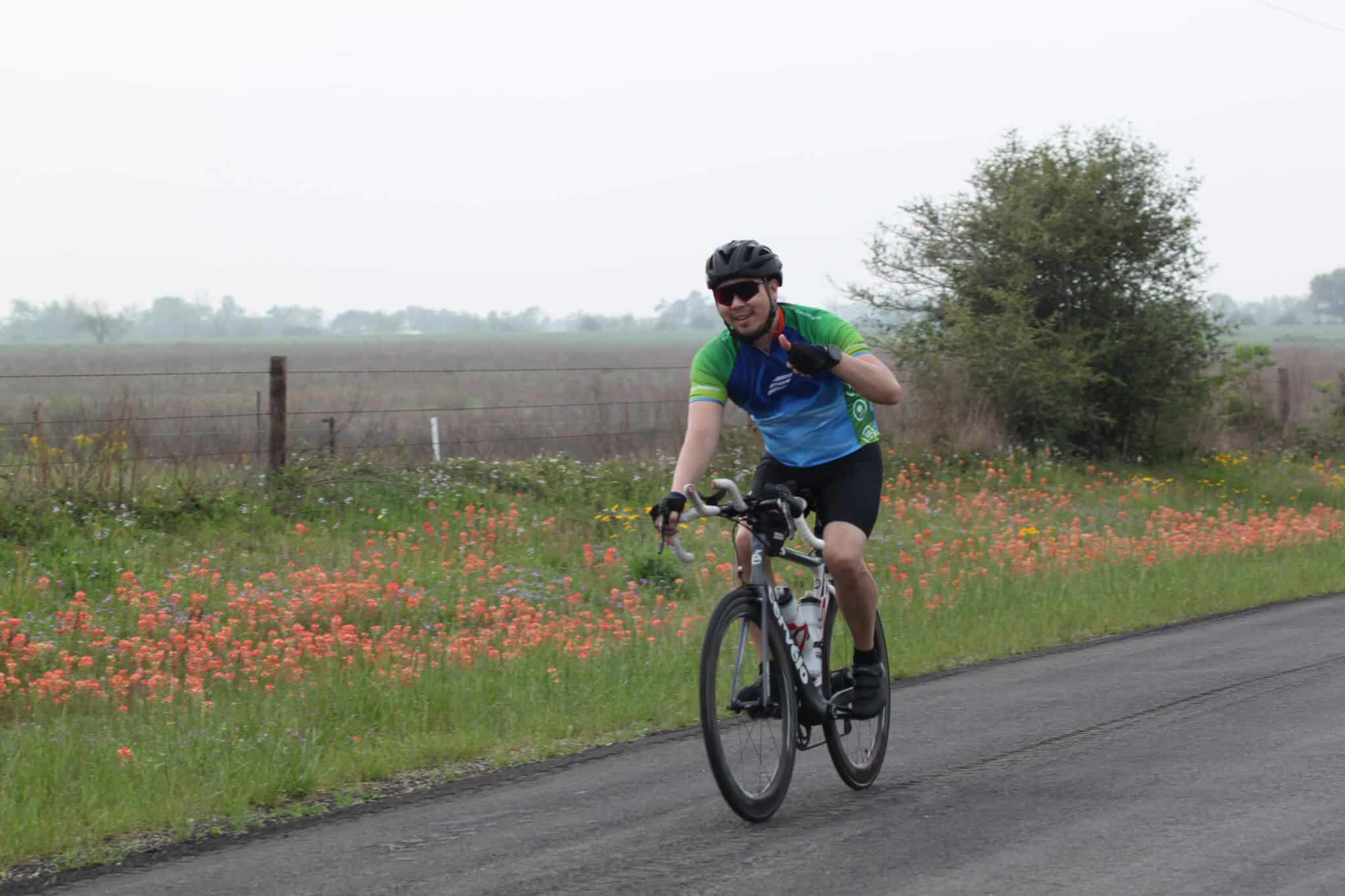 Vintage-style cyclist riding on a rural road with wildflowers, promoting Bluebonnet Express bike tours.