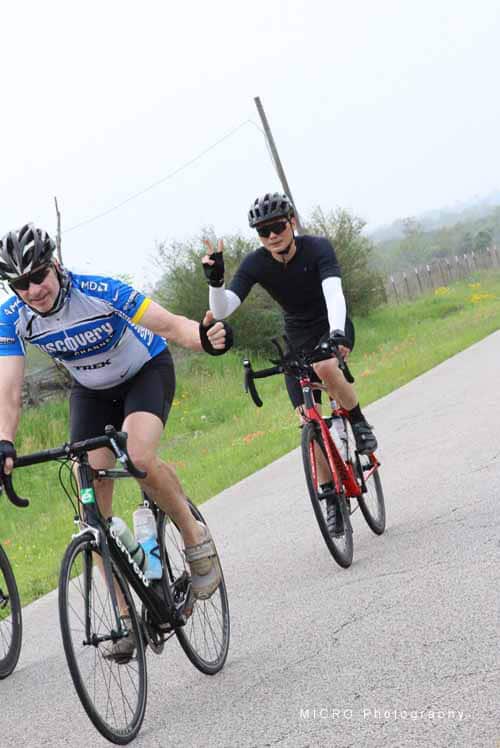 Cyclists riding on scenic road with green landscape, promoting Bluebonnet Express bike event.