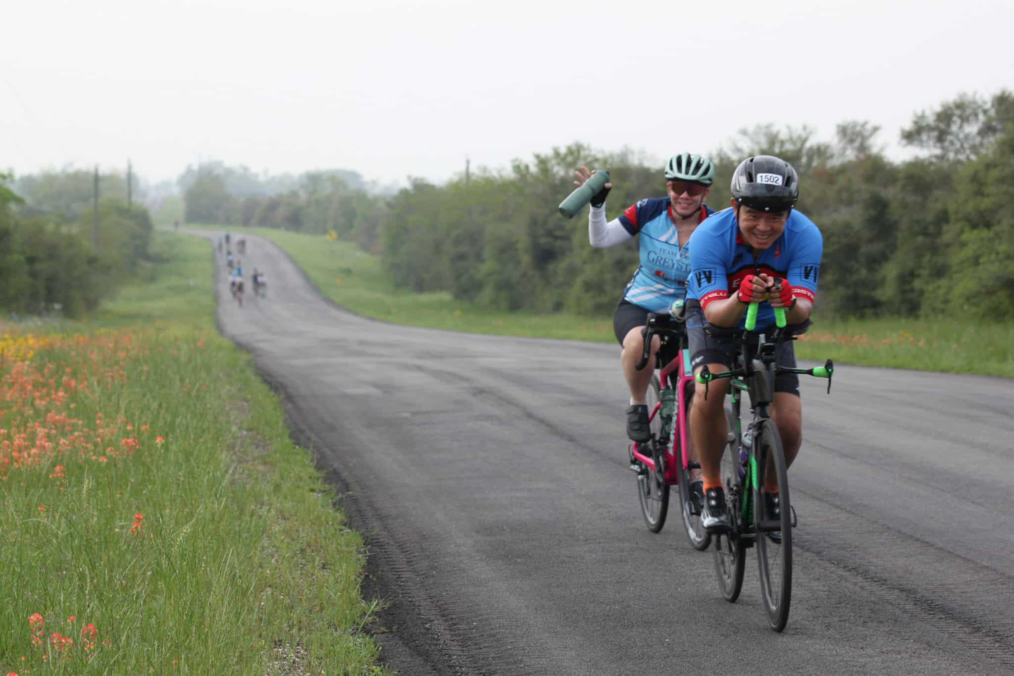 Fresh group of cyclists enjoying a scenic ride on a rural road with lush greenery and wildflowers.