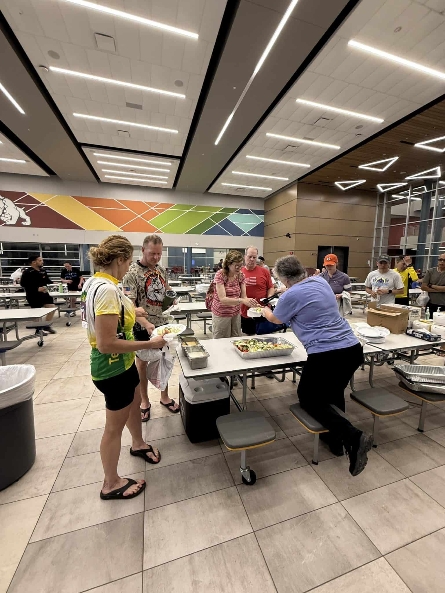 People enjoying a meal at a buffet table inside a modern, well-lit cafeteria or dining hall.