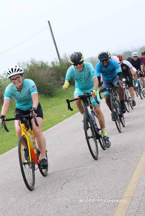 Riders in Bluebonnet Express cycling event wearing matching teal jerseys on a rural road.