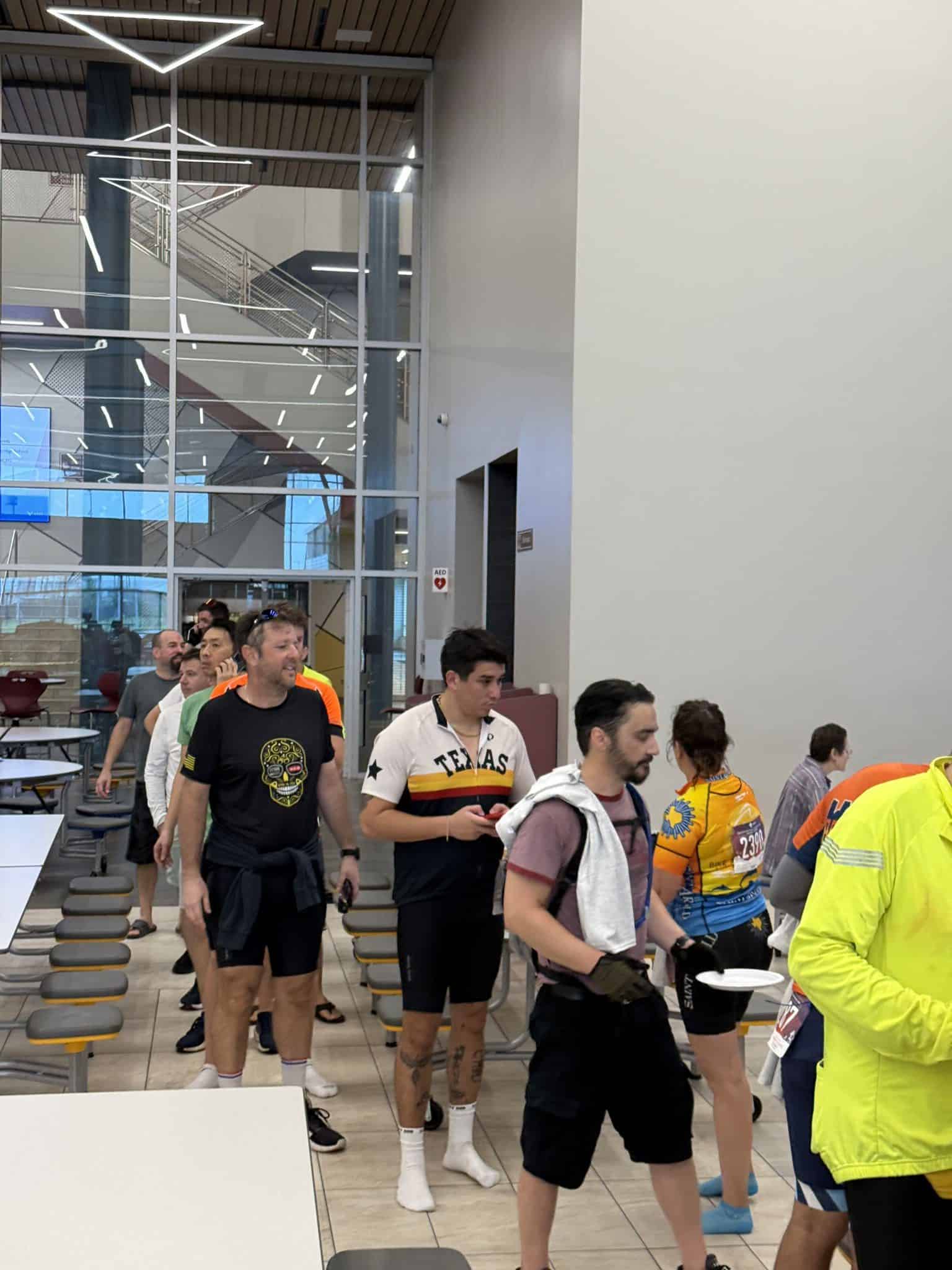 1. Diverse group of cyclists waiting indoors at Bluebonnet Express bike event.