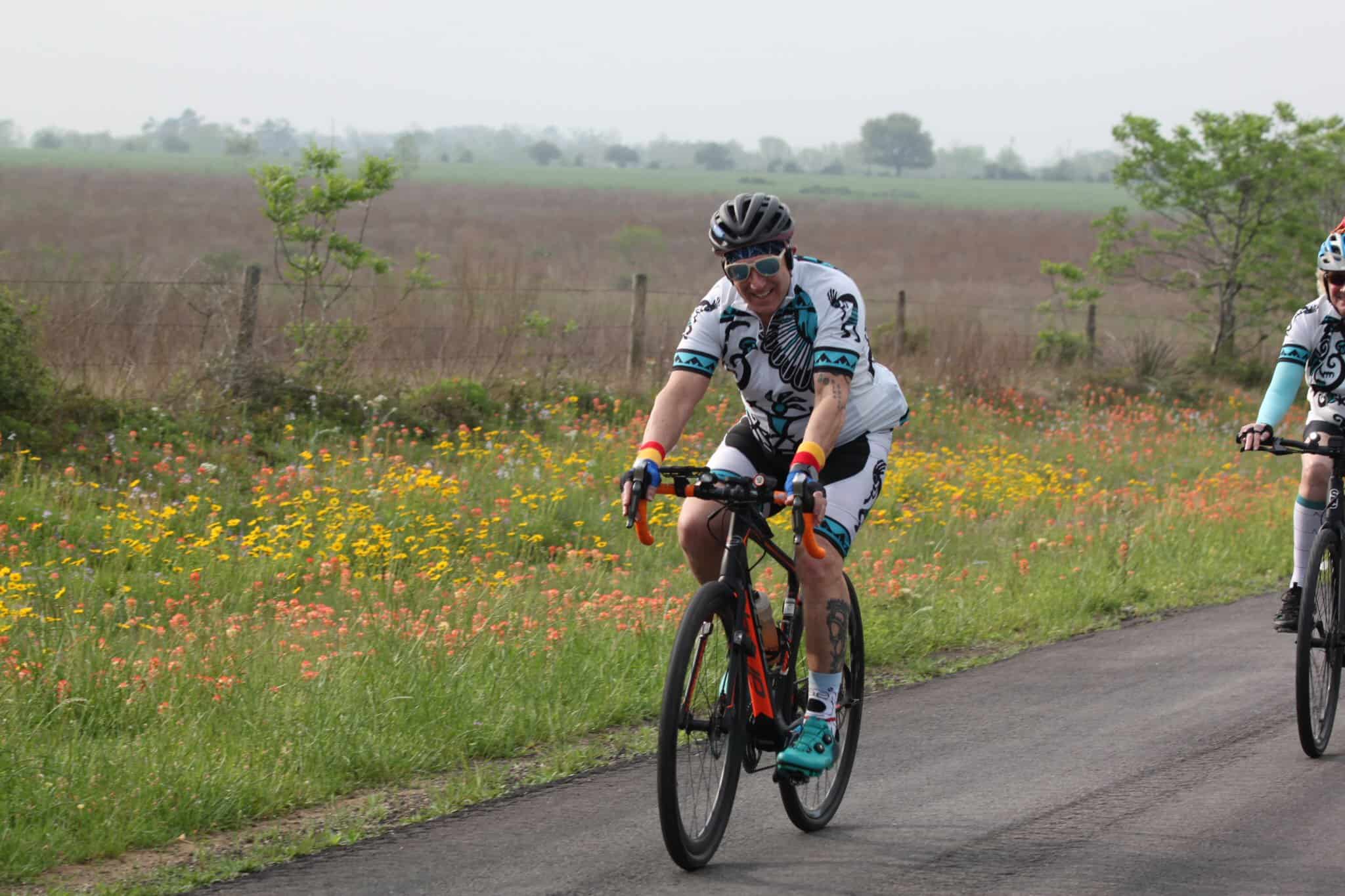 Vibrant cyclists riding on scenic countryside with wildflowers, promoting Bluebonnet Express bike tours and outdoor recreation.