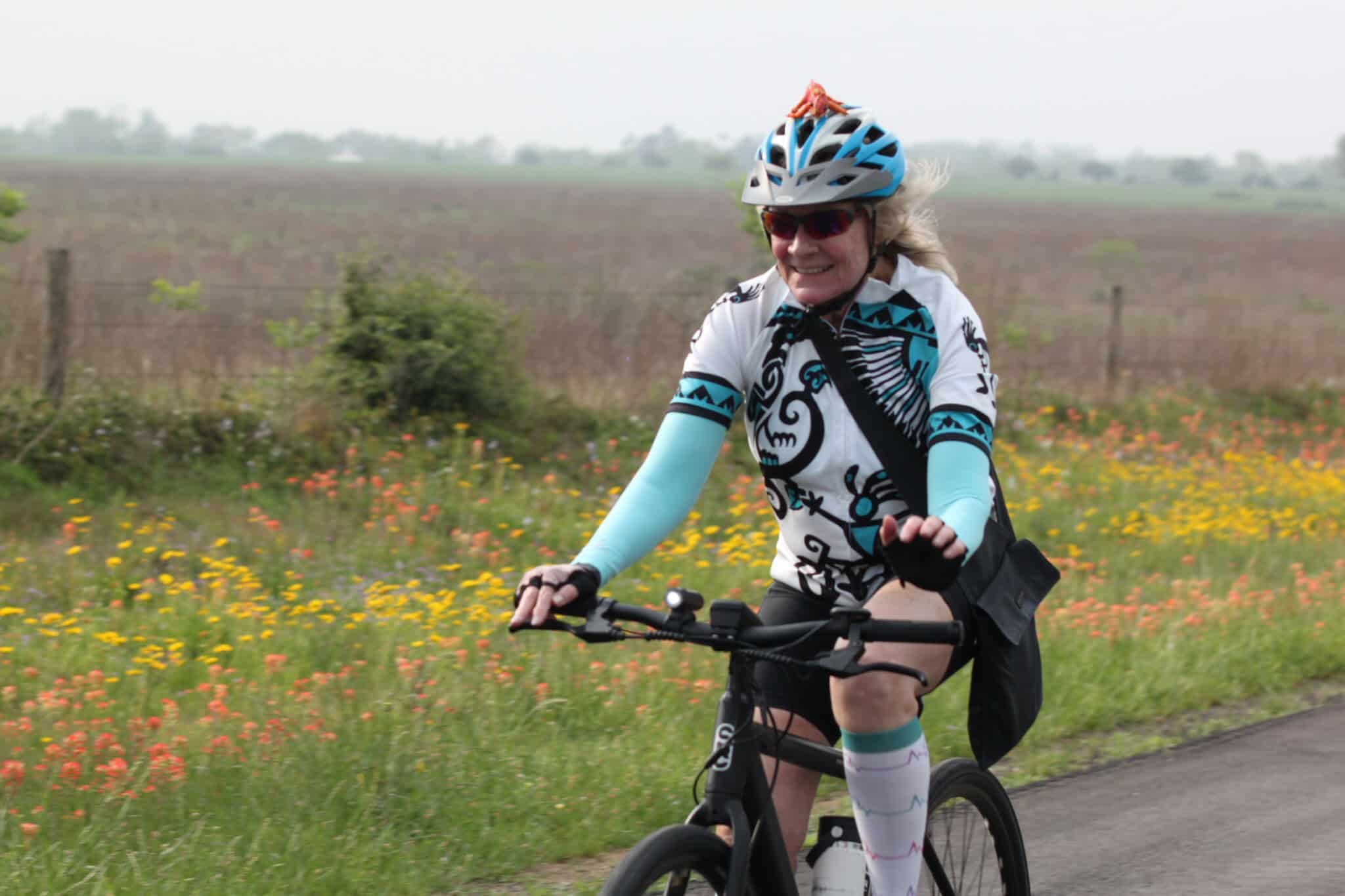 Vibrant woman cycling on scenic trail with colorful wildflowers for Bluebonnet Express event.