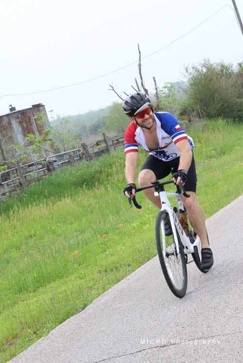 Bright cyclist with tree branches on helmet riding on scenic bike path during daytime.