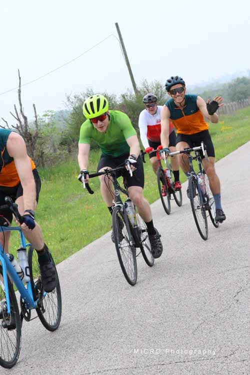 Brightly dressed cyclists riding on a scenic rural road for Bluebonnet Express event.