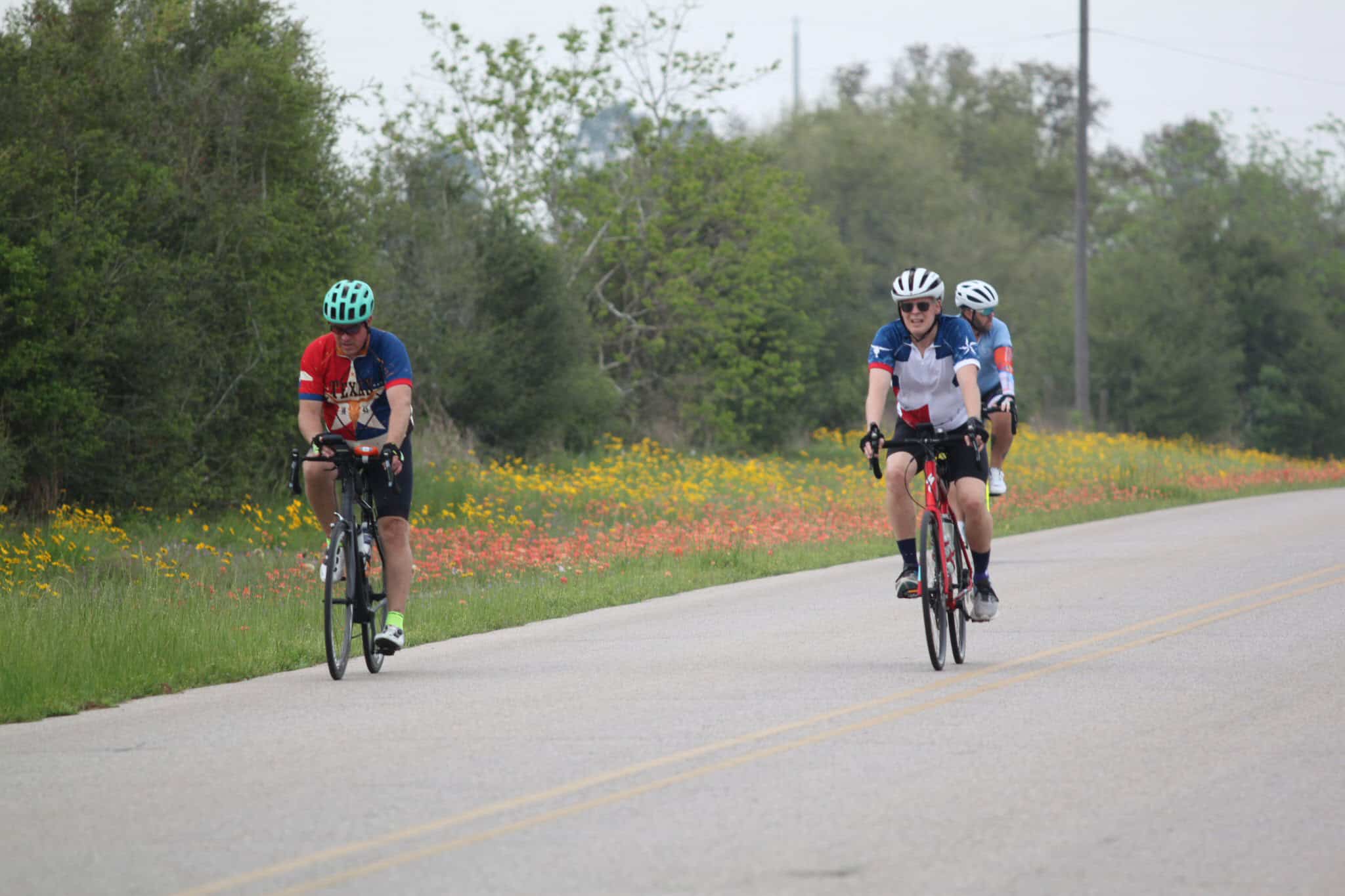 Bright blue and red cycling jerseys with helmets on Bluebonnet Express bike trail, scenic outdoor cycling adventure.