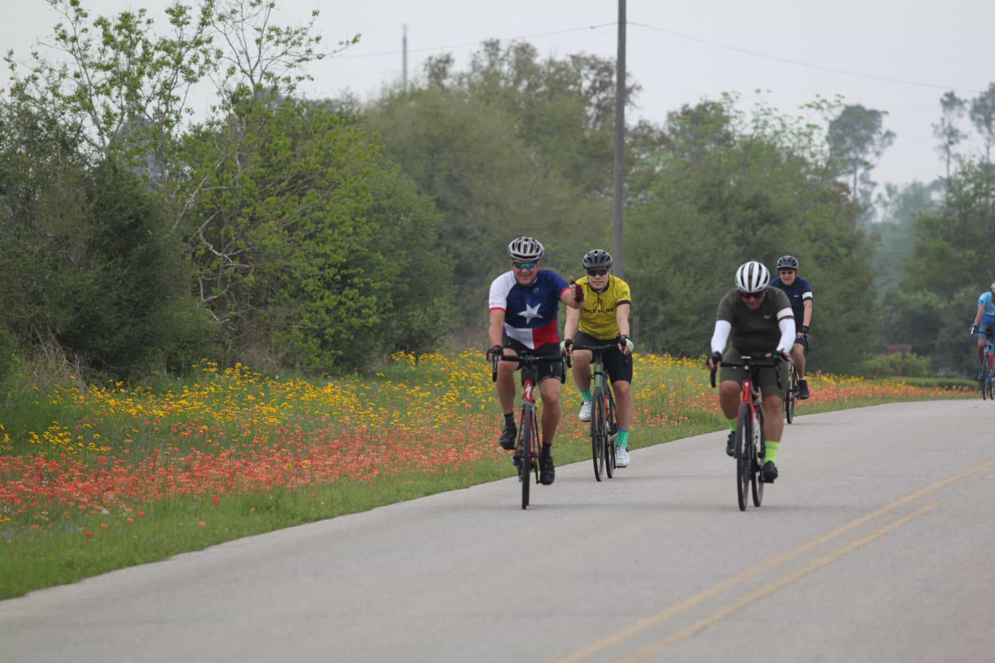 Bright cyclists riding on scenic country road during Bluebonnet season in Texas, showcasing outdoor biking adventure.