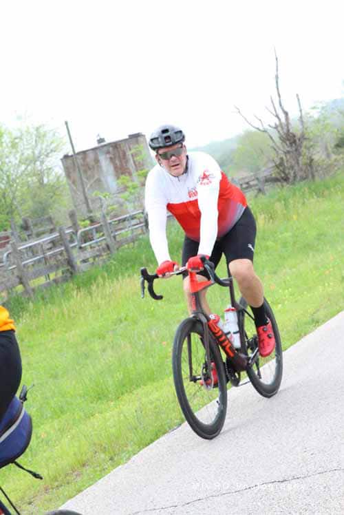 Rider on a road bike wearing a white and red cycling jersey, helmet, and sunglasses.