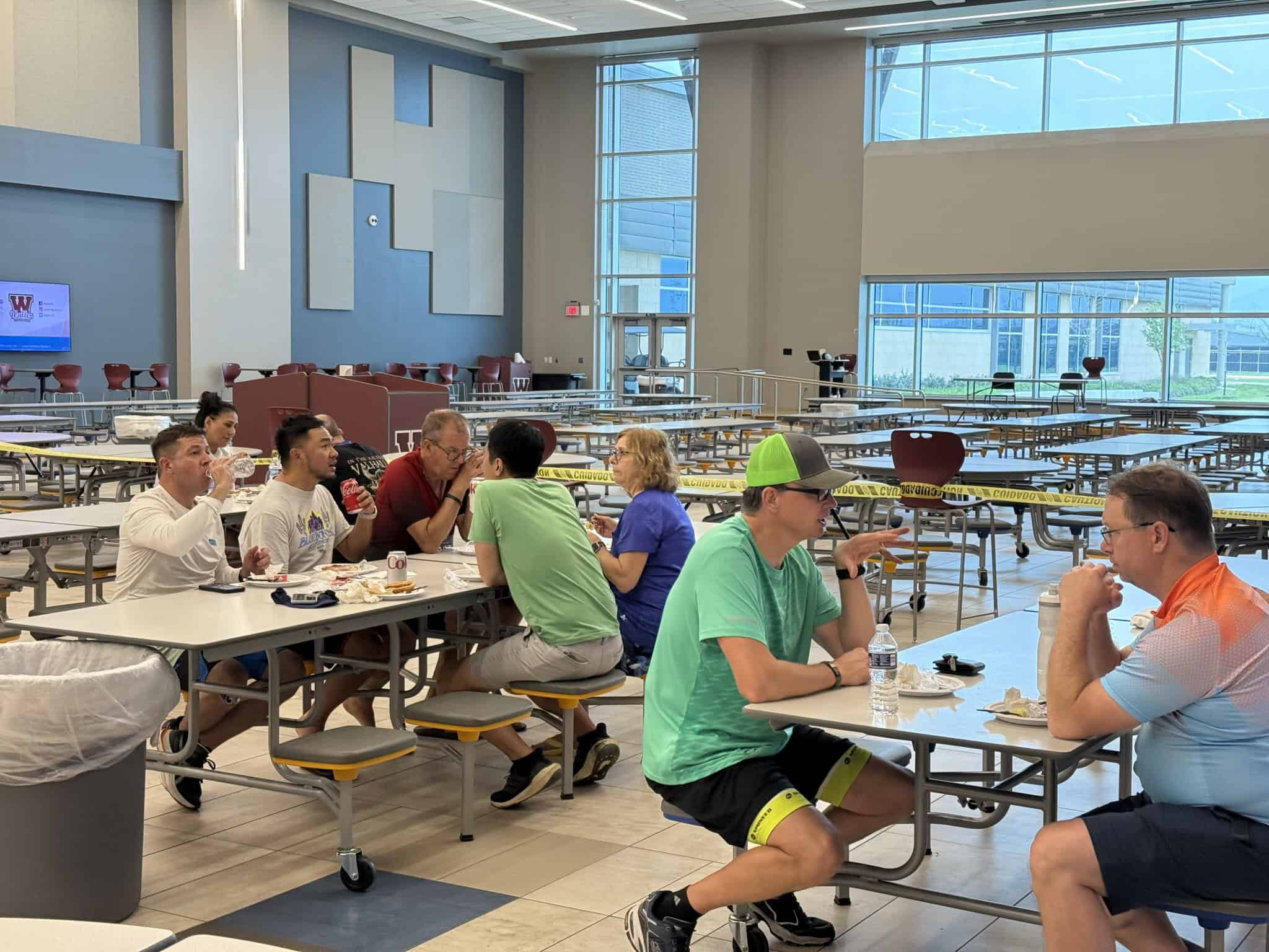 Multicultural group eating lunch in large modern cafeteria with high ceilings and large windows.