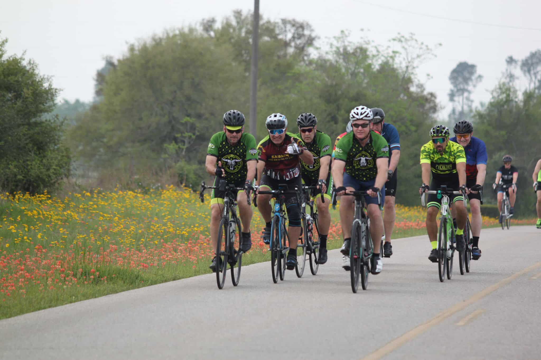 Bicycle group ride on scenic countryside road with colorful wildflowers, outdoor cycling event, Bluebonnet Express.