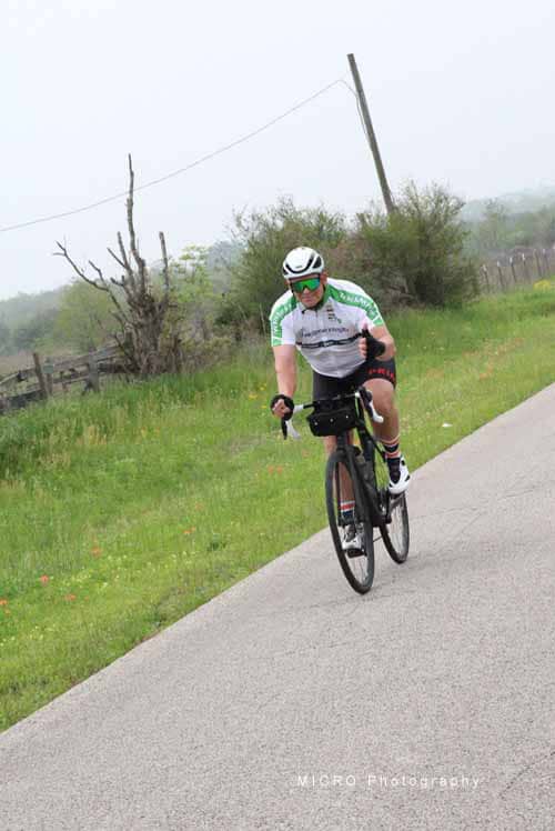 High-performance cyclist riding on a scenic rural road in challenging terrain.