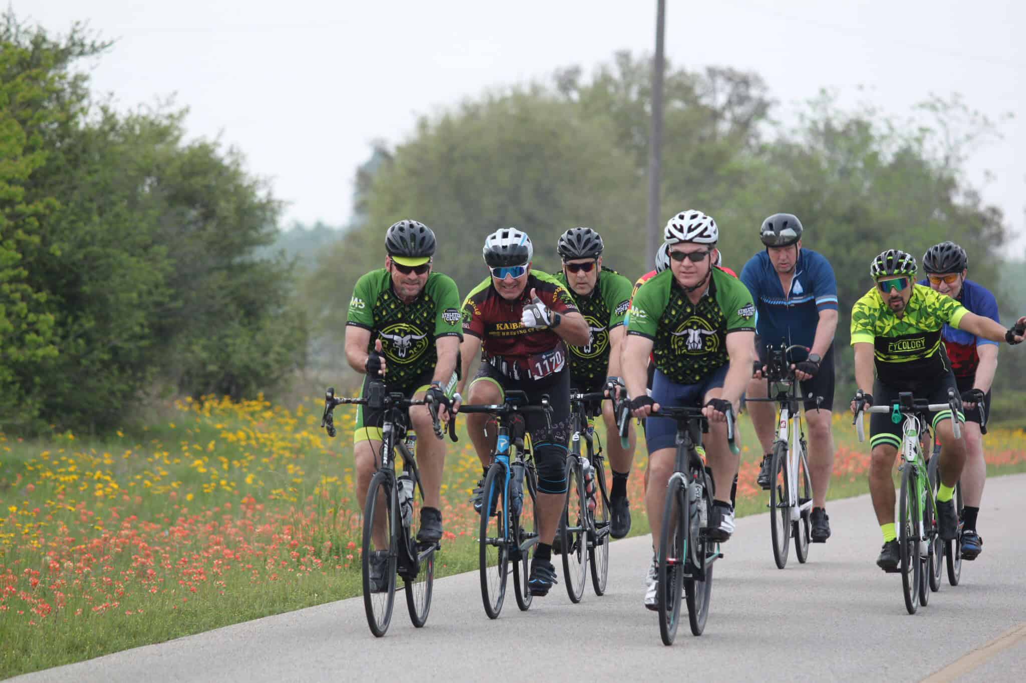 Vibrant group of cyclists riding through scenic countryside on Bluebonnet Express ride.