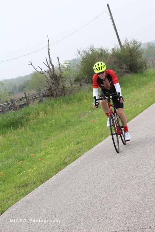 Bright yellow helmet cyclist riding on a rural paved trail during daytime.