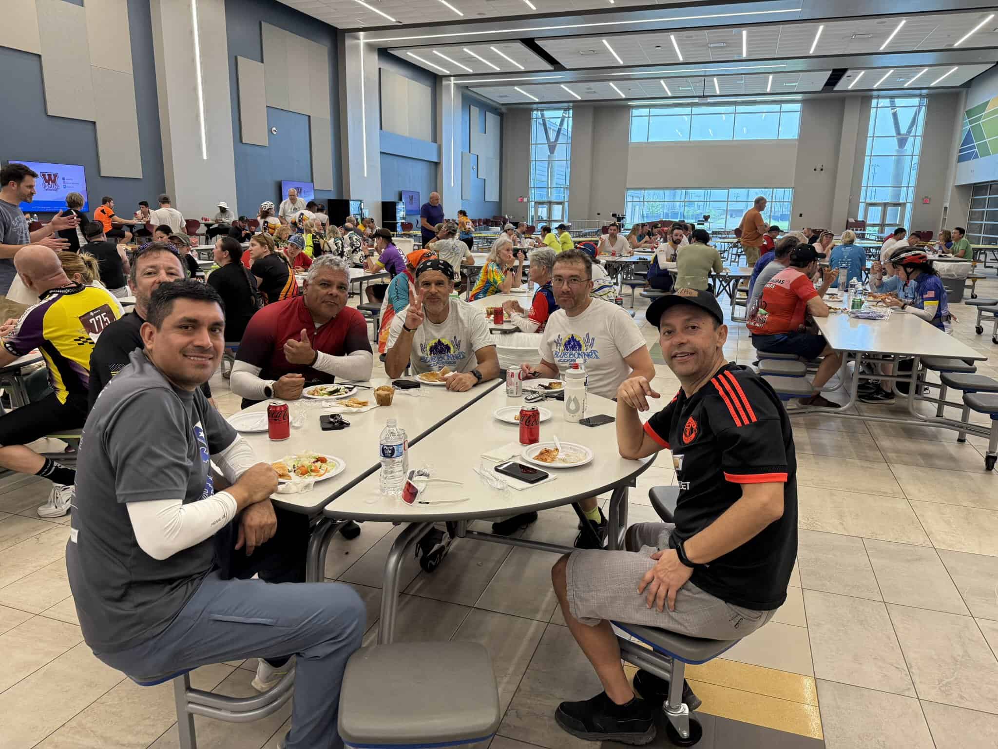 Joyful cyclists enjoying a meal at Bluebonnet Express event in a modern, spacious atrium with large windows.