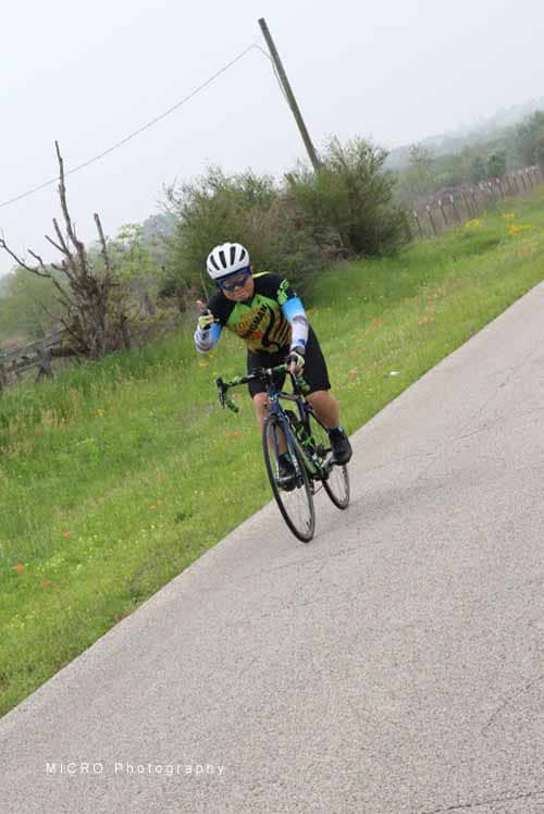 Cyclist riding on scenic rural road with greenery and overcast sky during Bluebonnet Express event.