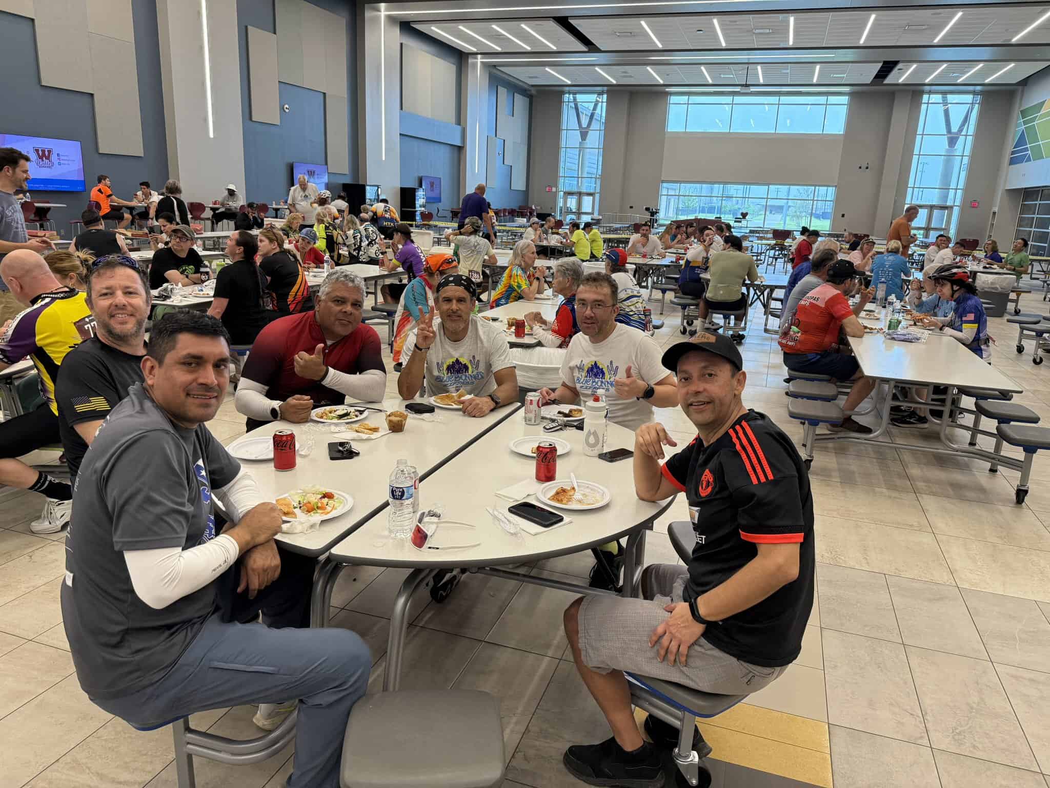 Busy indoor dining area at Bluebonnet Express cycling event with diverse participants enjoying meals.