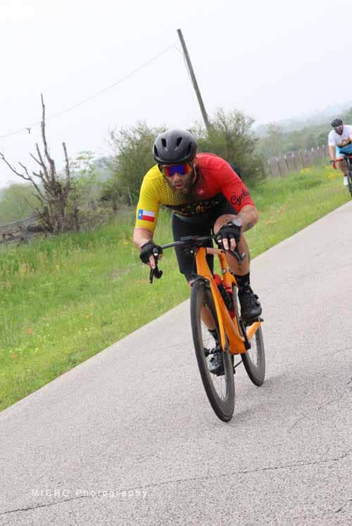 Velo cyclist in red and yellow jersey riding on rural road during bike race.