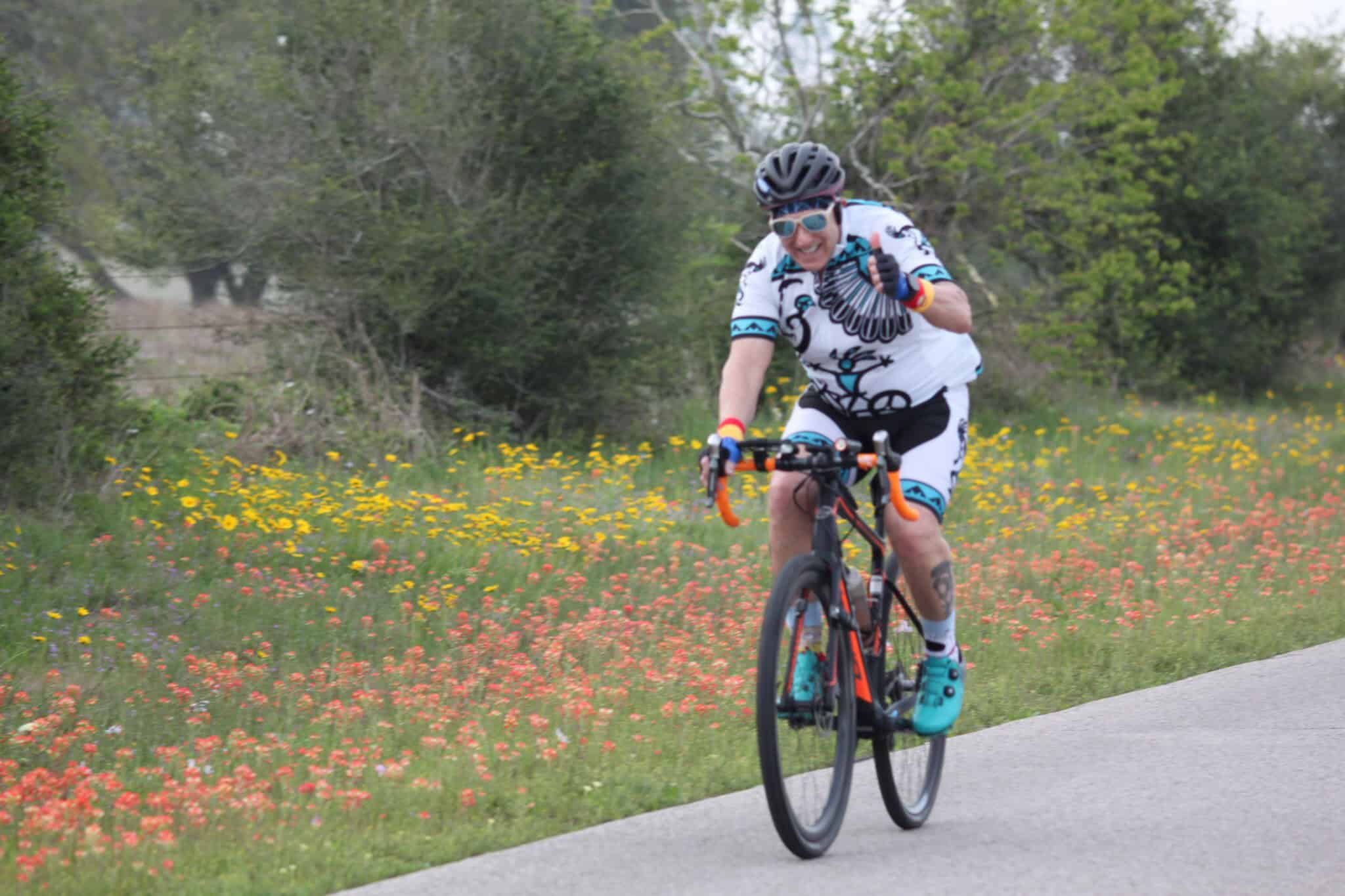 Bright cyclist smiling on a scenic floral trail with Bluebonnet Express branding in the background.
