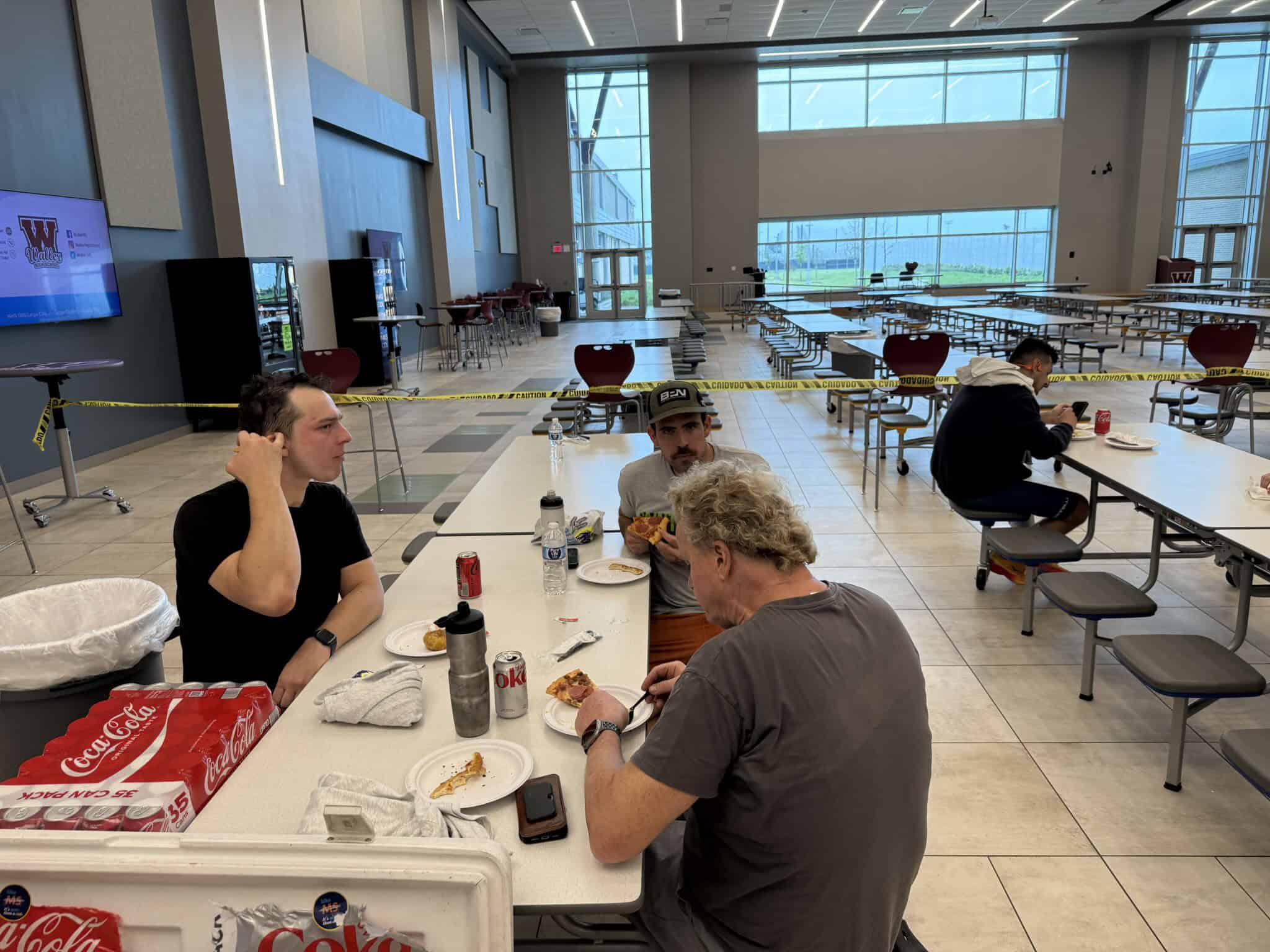 Empty dining hall with a few people eating, spacious modern interior, high glass windows, social distancing measures in place.