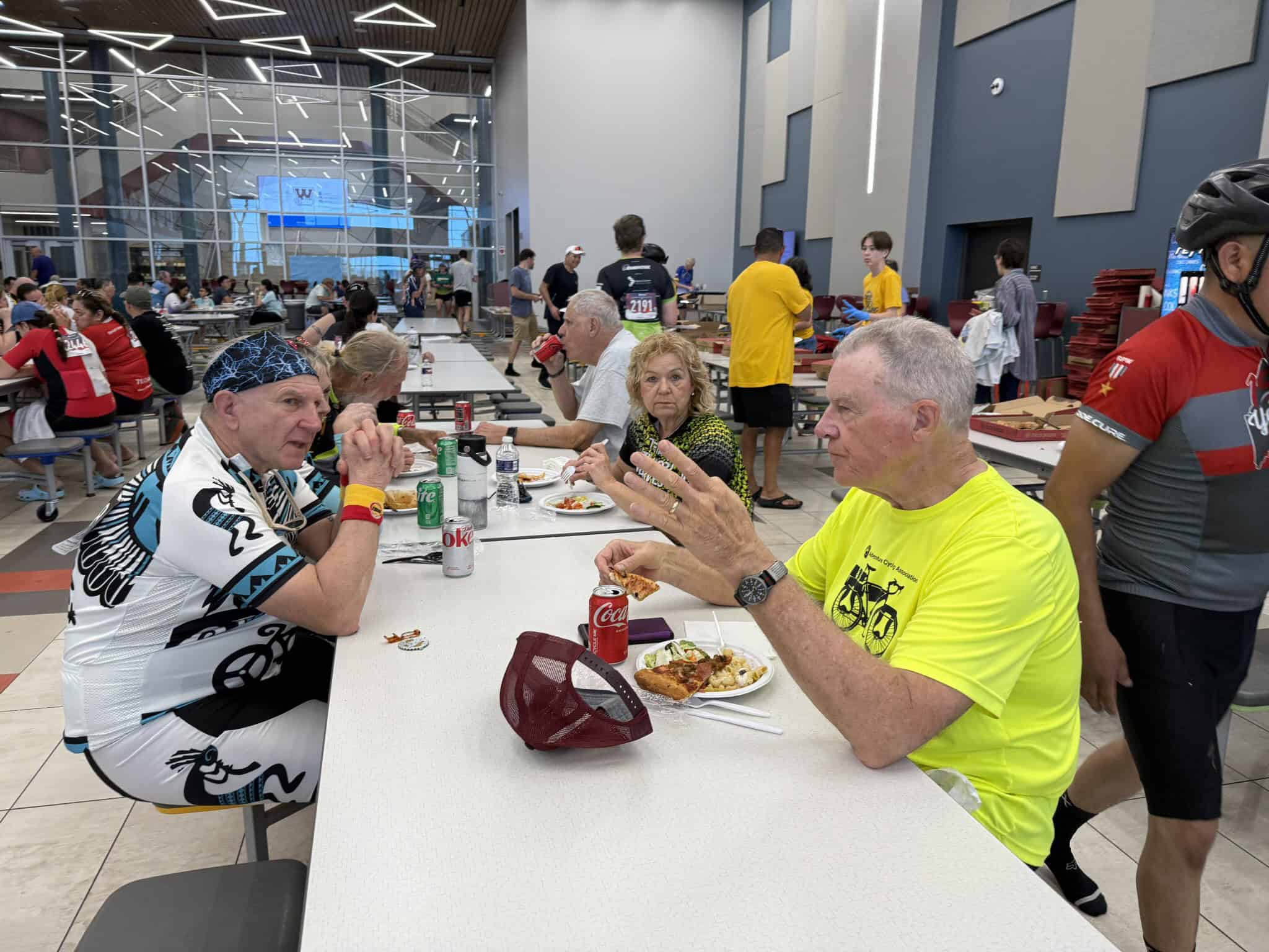 Cyclists enjoying a meal at Bluebonnet Express cycling event, large indoor dining area, camaraderie, and race support.