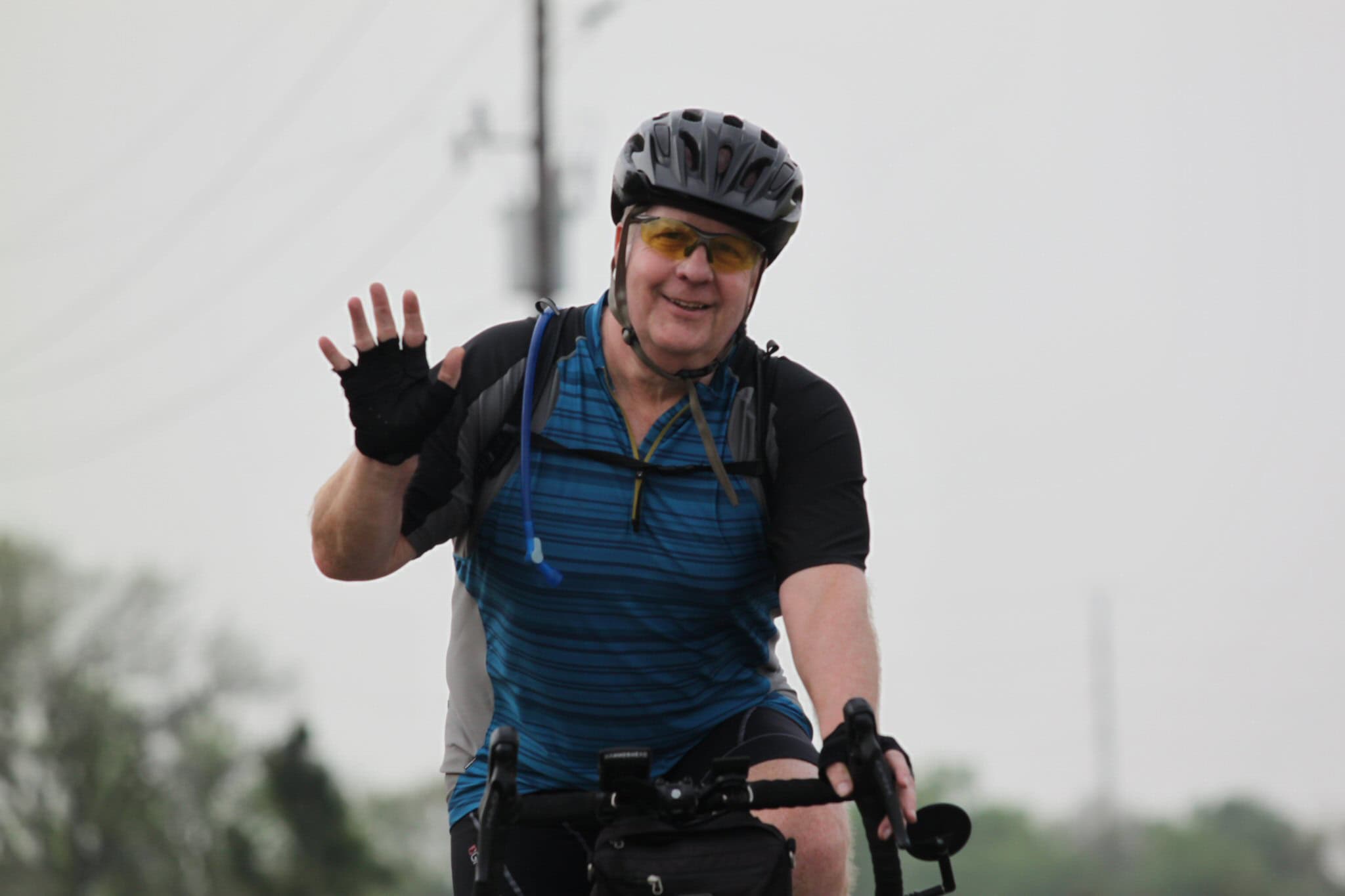 Smiling man cycling, wearing helmet and sunglasses, enjoying Bluebonnet Express ride.