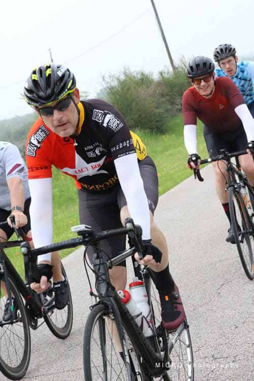 Vibrant cyclist group riding on scenic outdoors road during daytime.