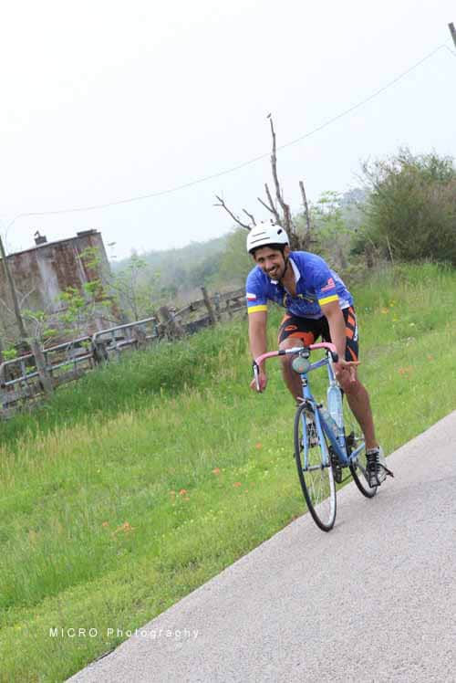 Bright blue cyclist jersey, wearing helmet, riding road bike on scenic countryside path.