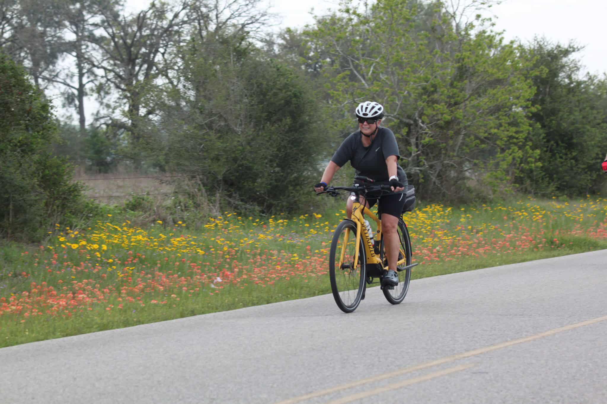 Bright woman cycling on scenic road with flowers and greenery for Bluebonnet Express adventure.