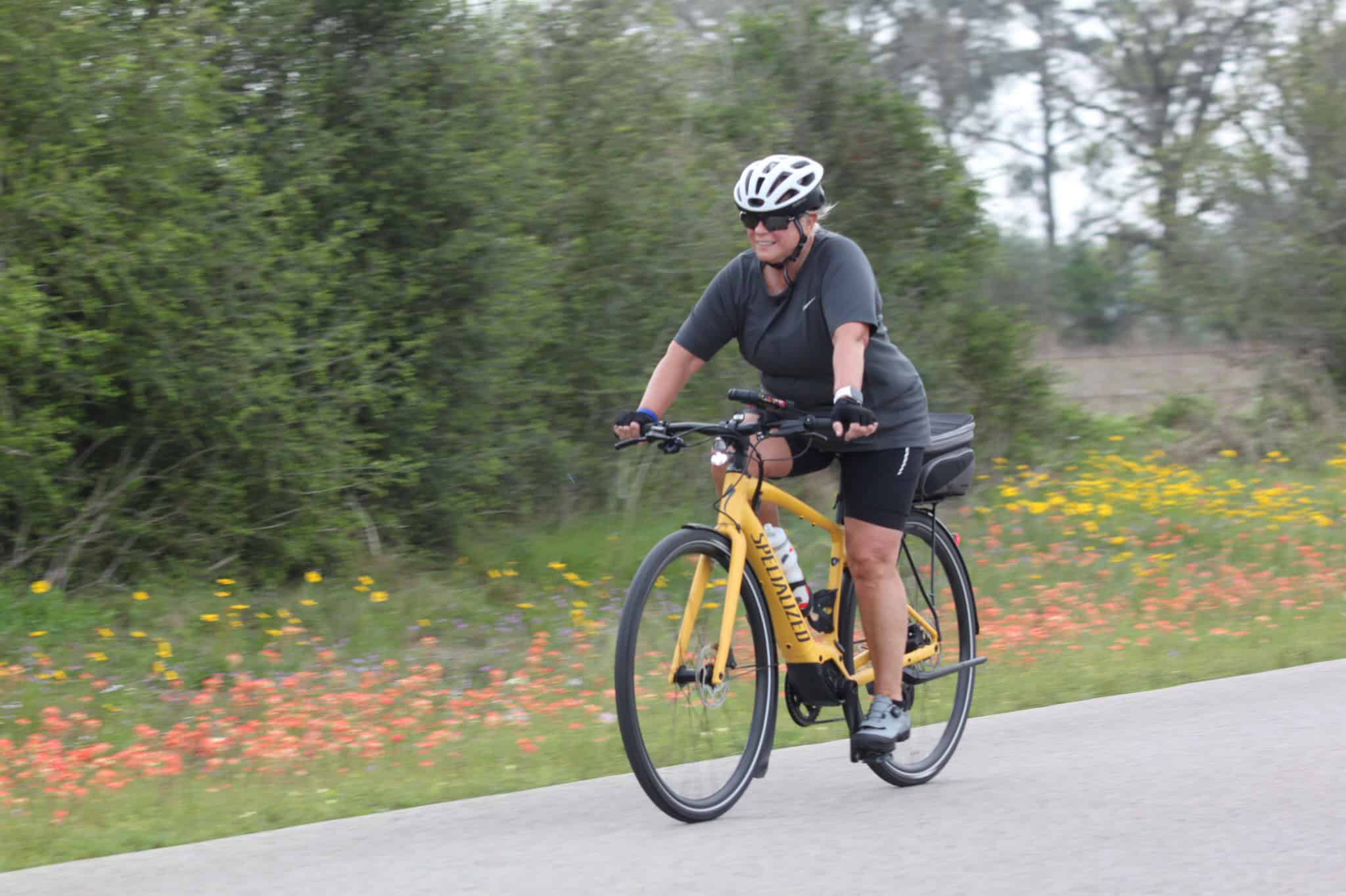 Bright yellow electric bicycle on scenic trail with lush greenery and wildflowers.