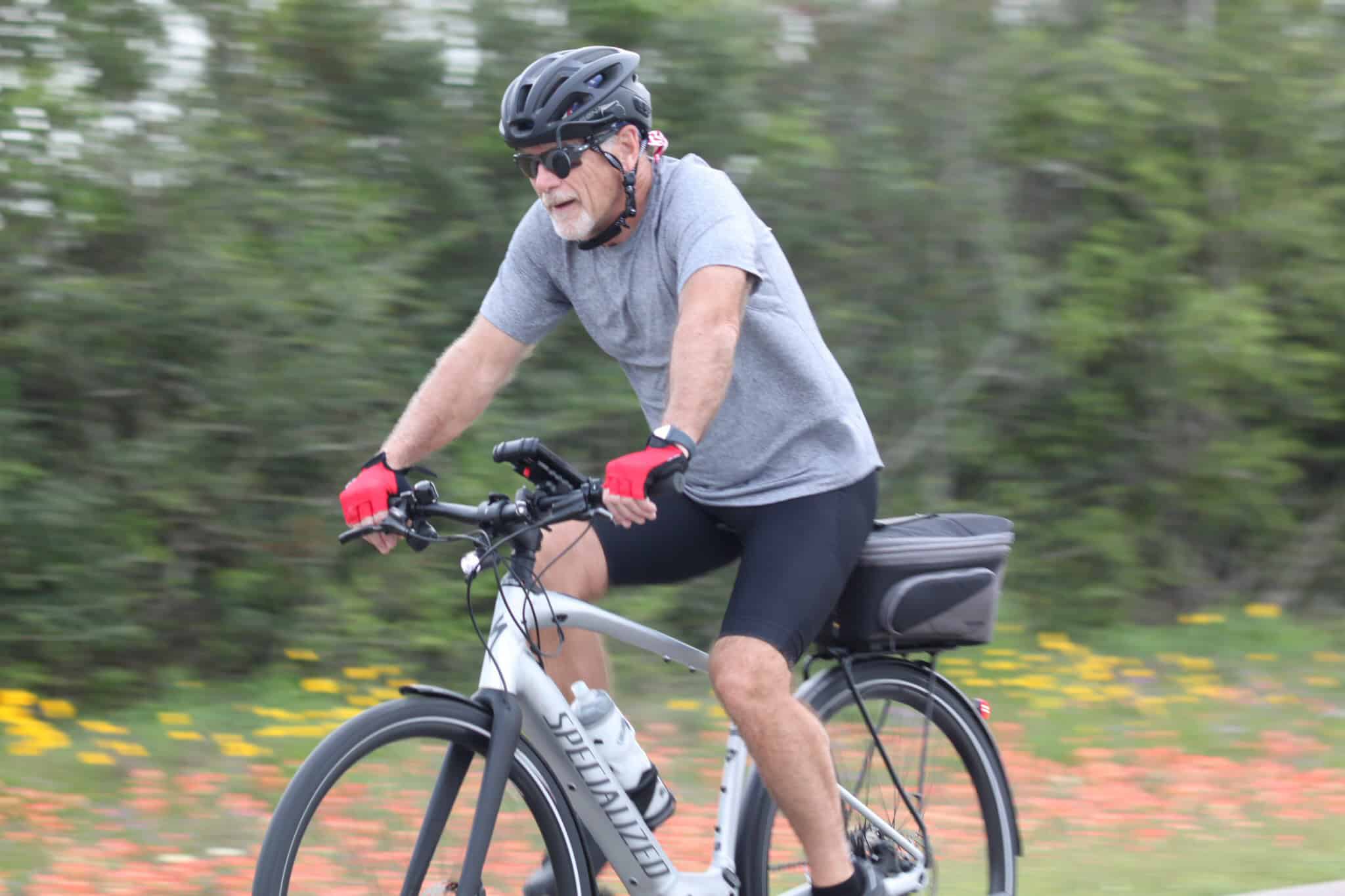 Elder man riding a Specialized e-bike in a natural outdoor setting with green foliage.