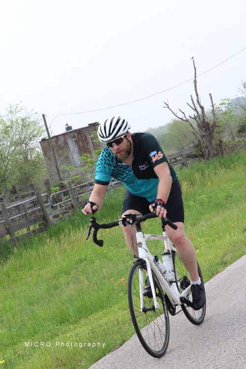 Rider on a road bike cycling through a scenic rural landscape with trees and a rustic barn.
