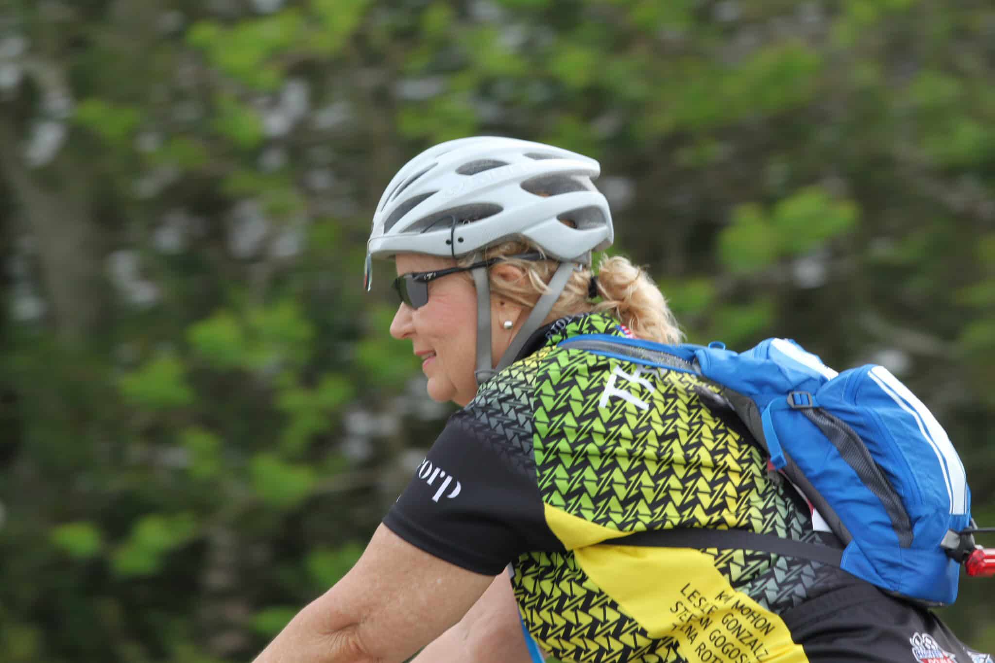 Women cyclist with helmet and colorful jersey riding outdoors on a trail.