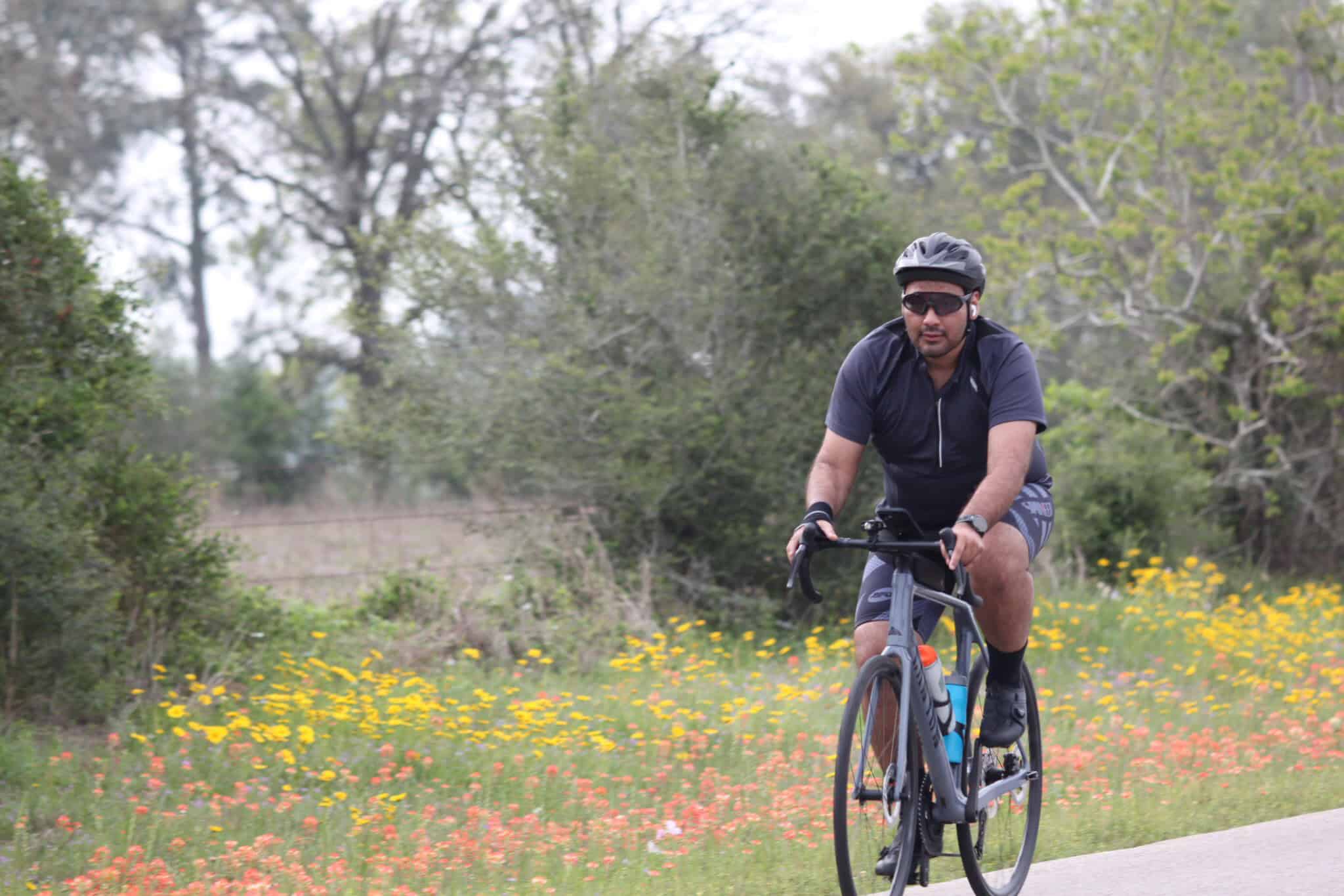 Man cycling in scenic outdoor trail with colorful flowers and lush greenery for Bluebonnet Express.