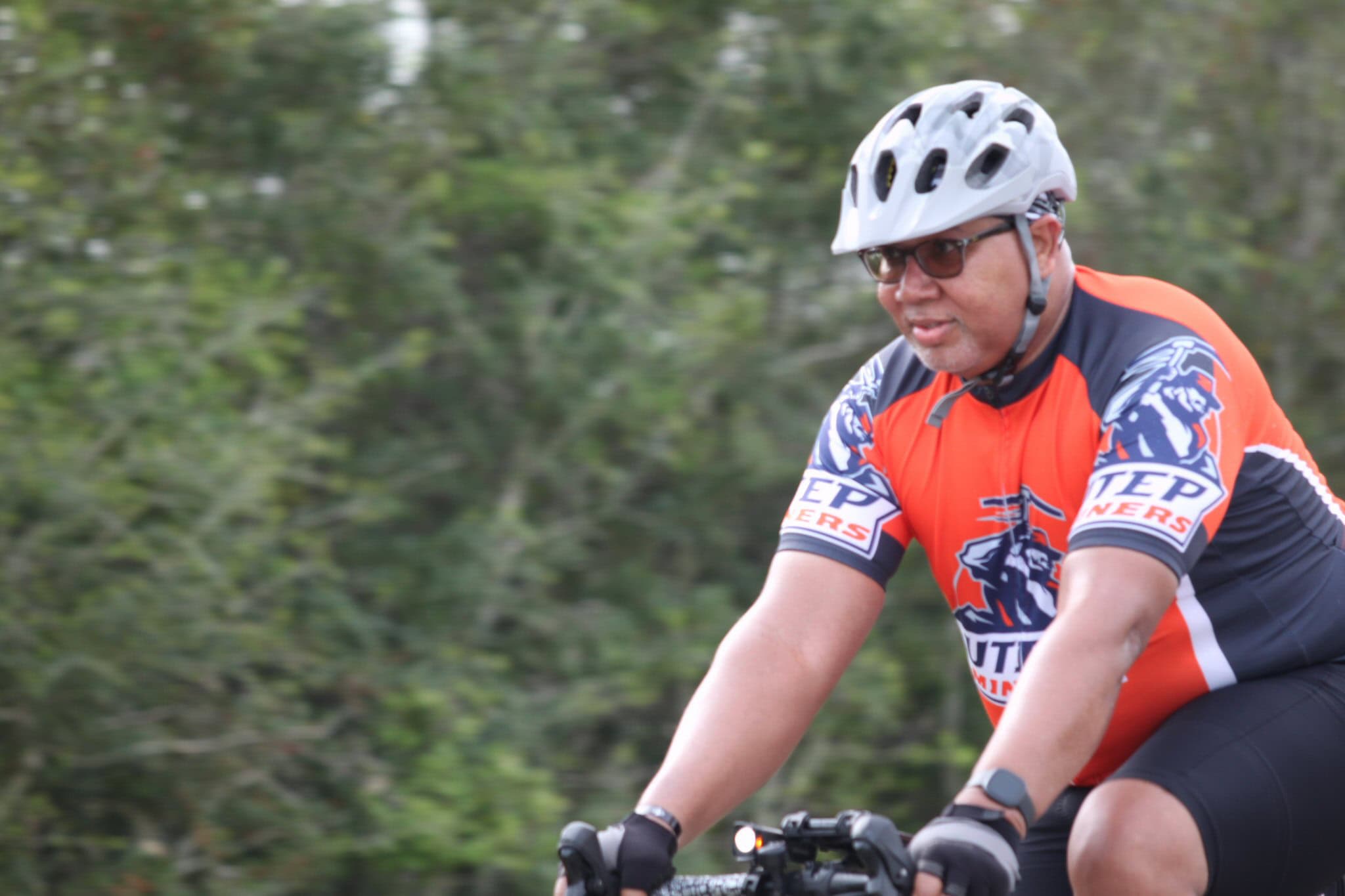 Man riding bicycle outdoors in cycling gear with Green forest background.