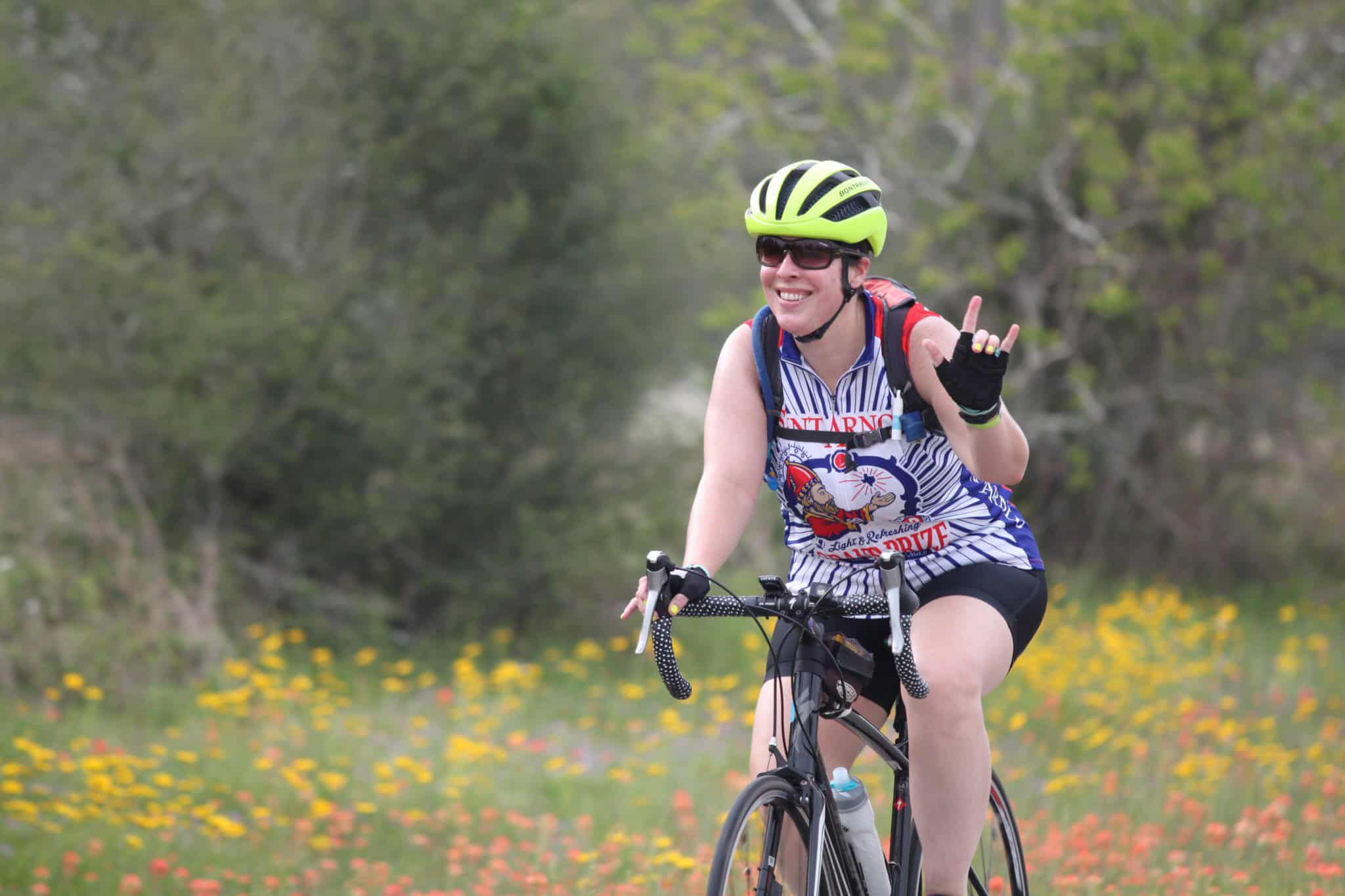 Bright yellow bike helmet, smiling woman cycling outdoors, celebrating triumph in scenic nature.