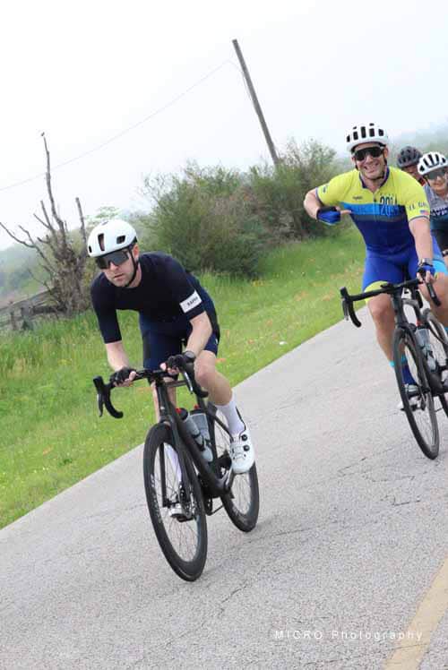 Riders cycling on scenic rural road during Bluebonnet Express event, promoting outdoor biking and Texas countryside.
