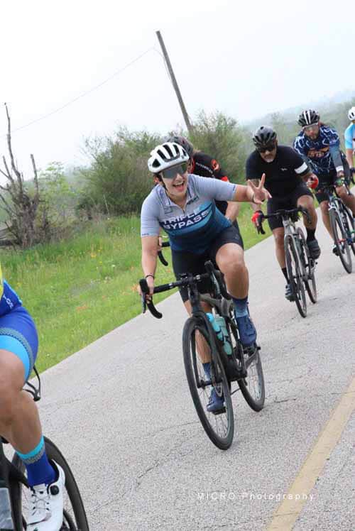 Bright smiling female cyclist making peace sign during Bluebonnet Express group bike ride in Texas.