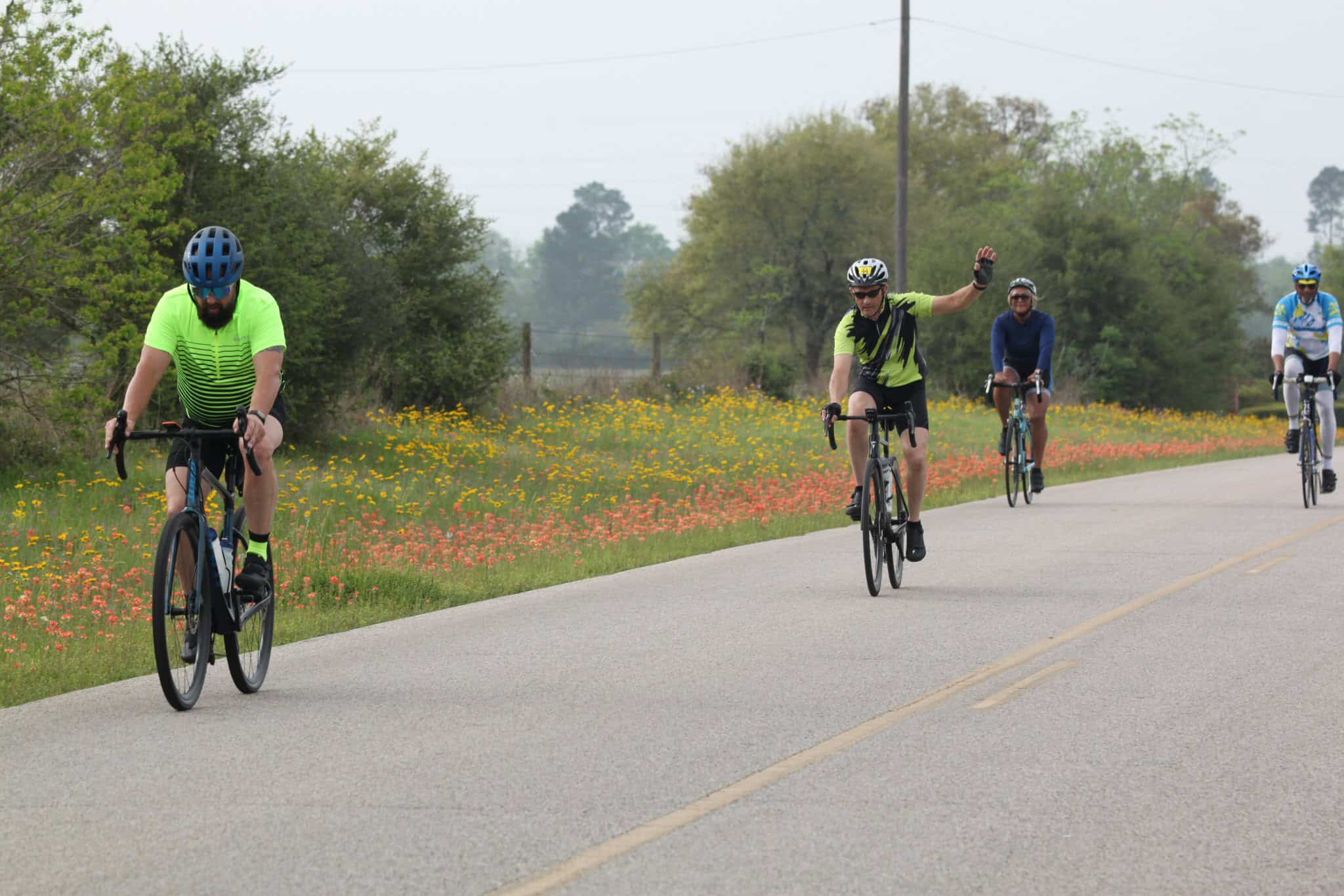 Cyclists riding on scenic rural road with wildflowers, promoting Bluebonnet Express bike tours and outdoor cycling adventures.